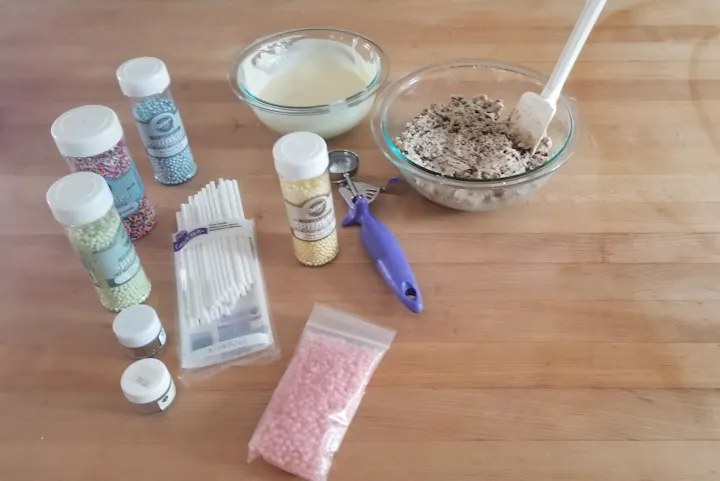 a photo showing all the ingredients to make and decorate edible cookie dough pops.