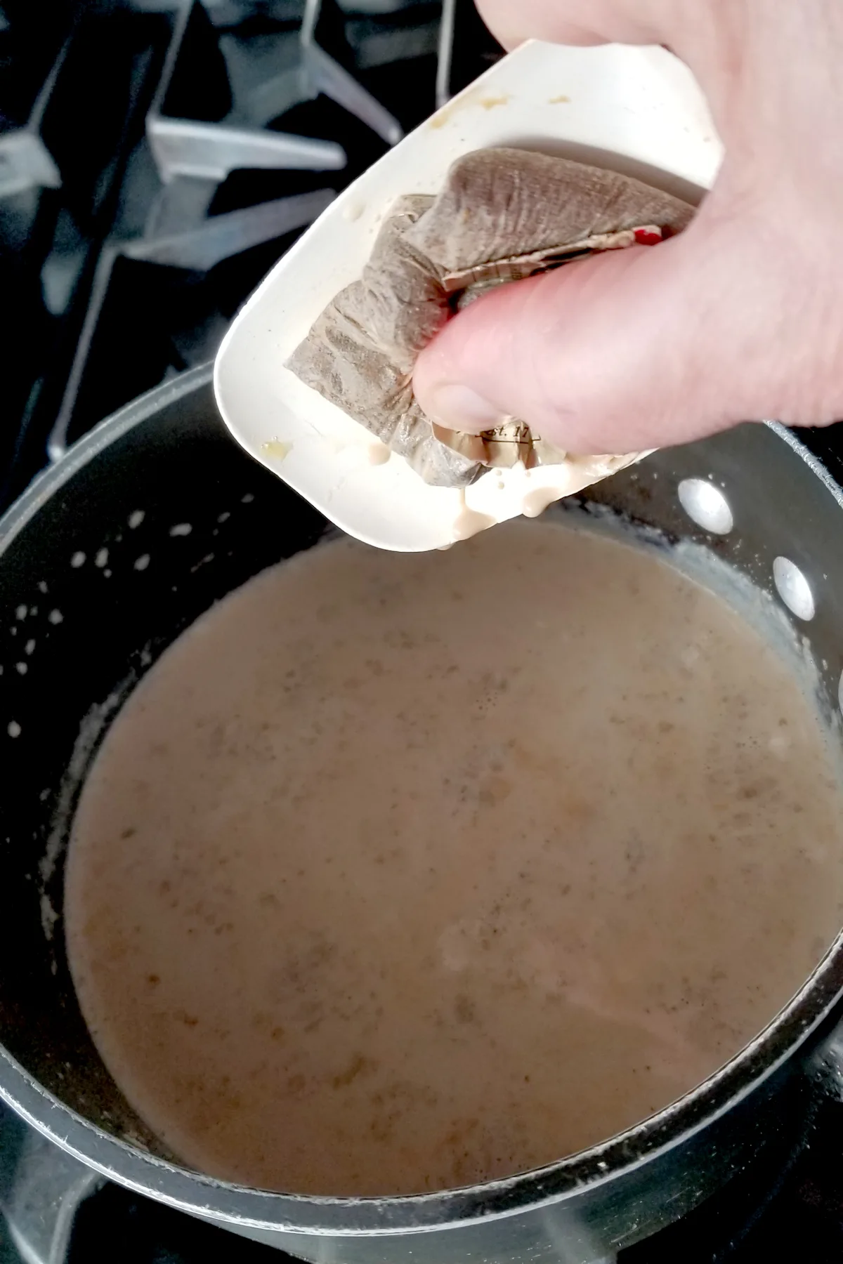 a pot of chai ice cream on a stove and a hand squeezing a tea bag over the pot.