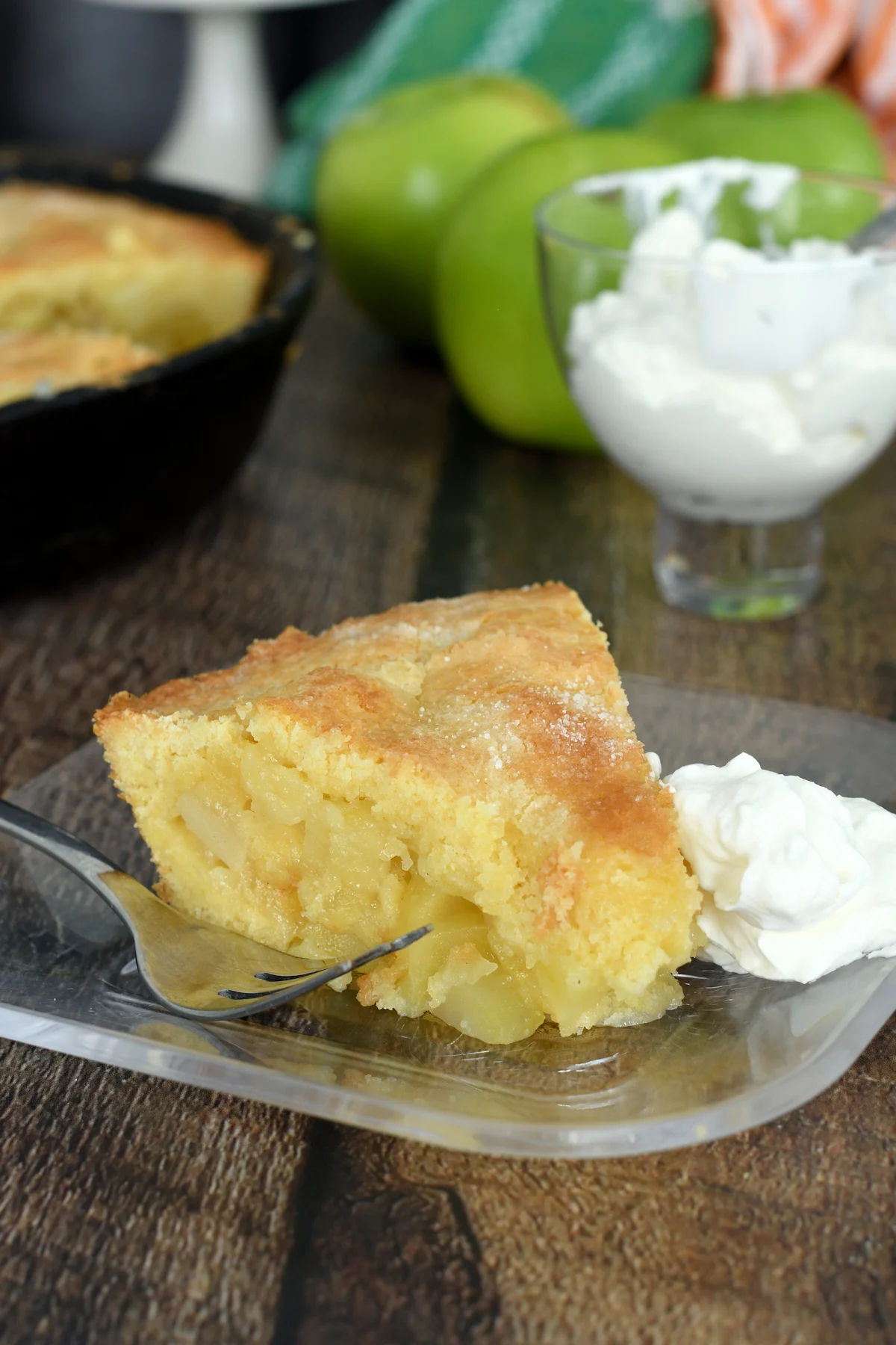 a slice of irish apple cake on a glass plate with whipped cream.