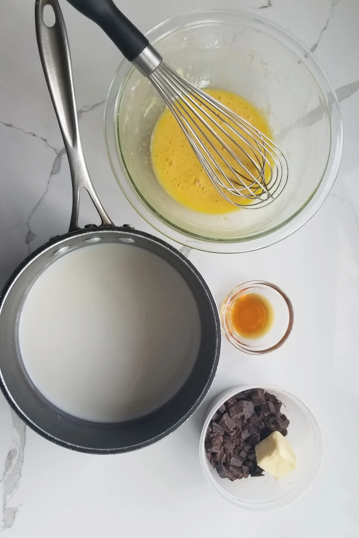 eggs in a bowl, milk in a saucepan, vanilla in a bowl and chocolate and butter in a bowl.