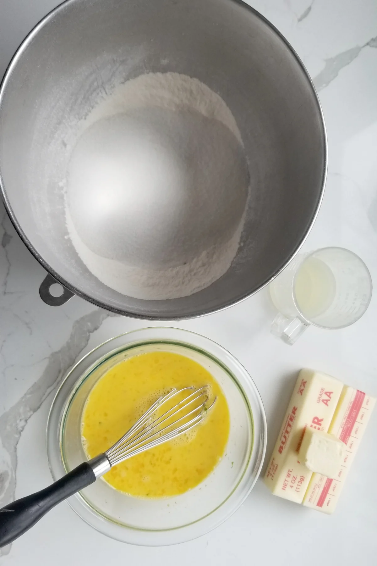 A mixing bowl with dry ingredients, a small bowl with egg mixture, a cup with lime juice and 2 sticks of butter.