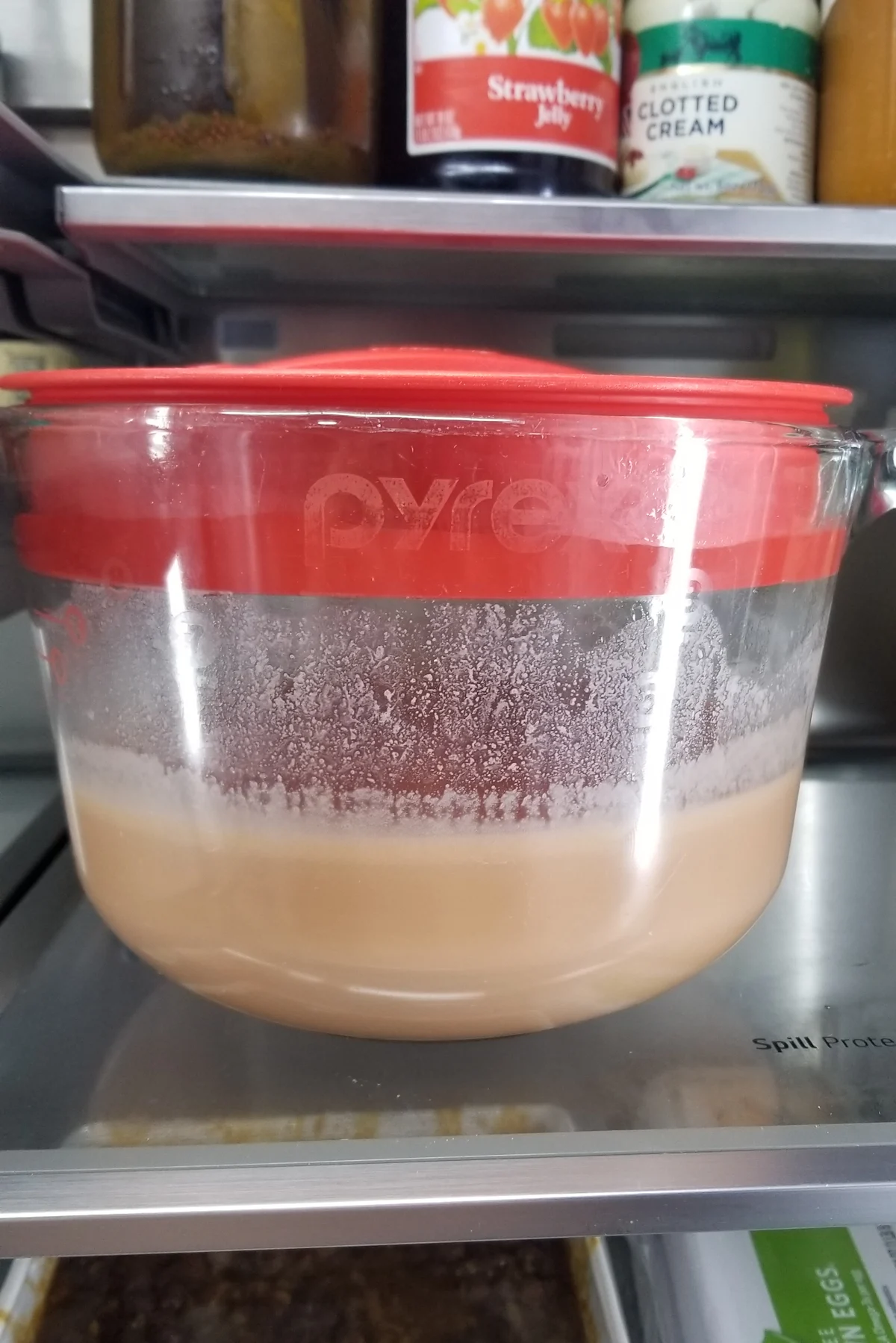 a large glass measuring cup of custard on a refrigerator shelf.