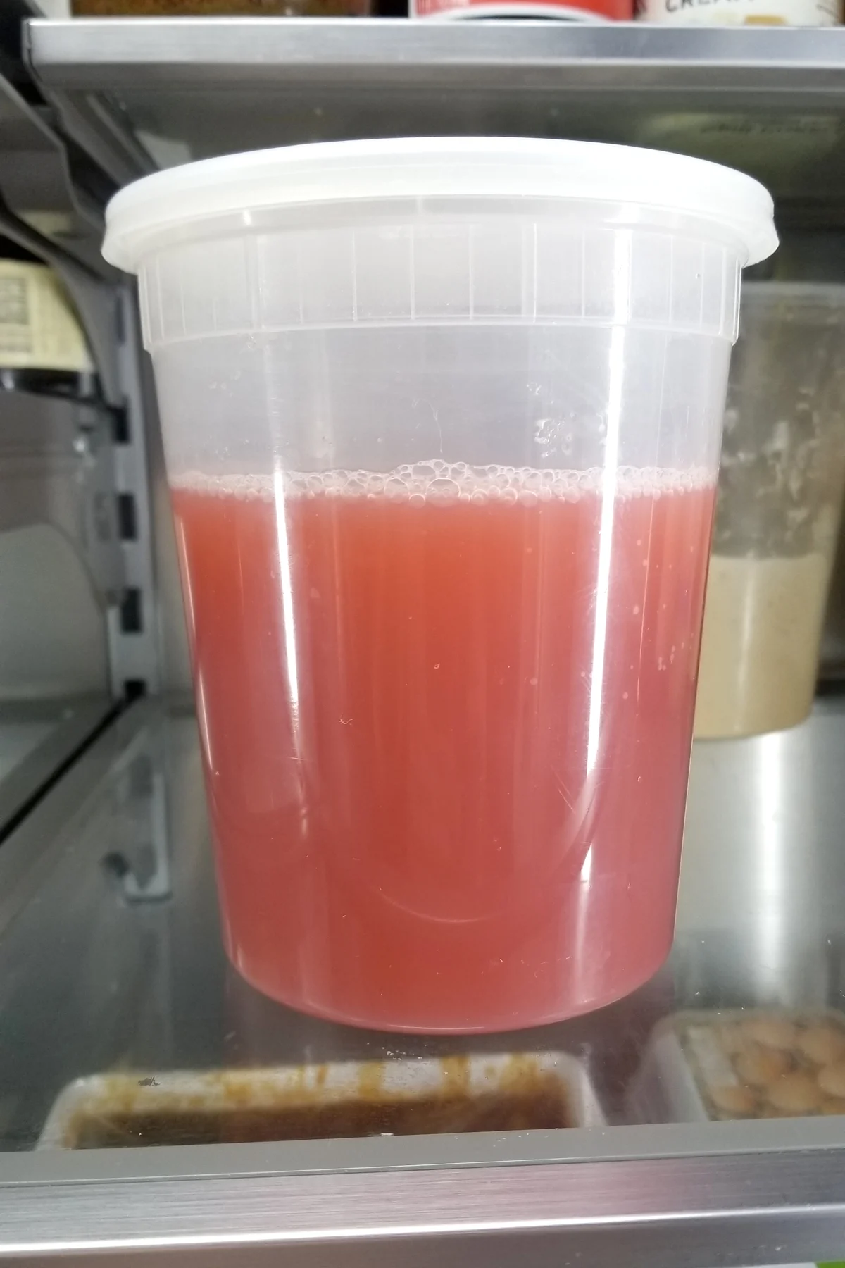 a plastic deli container filled with rhubarb syrup in a refrigerator.