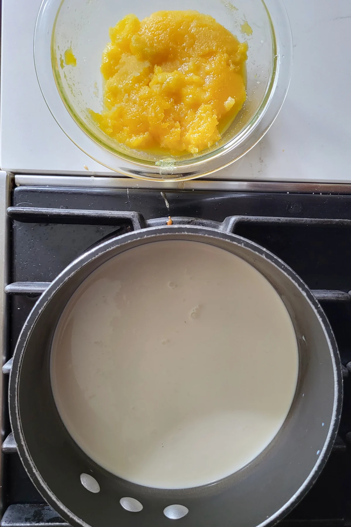 a bowl of egg yolks and a pan filled with cream on the stove.