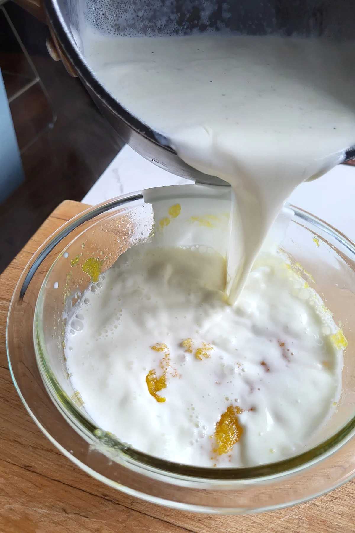hot cream pouring into a bowl of egg yolks.