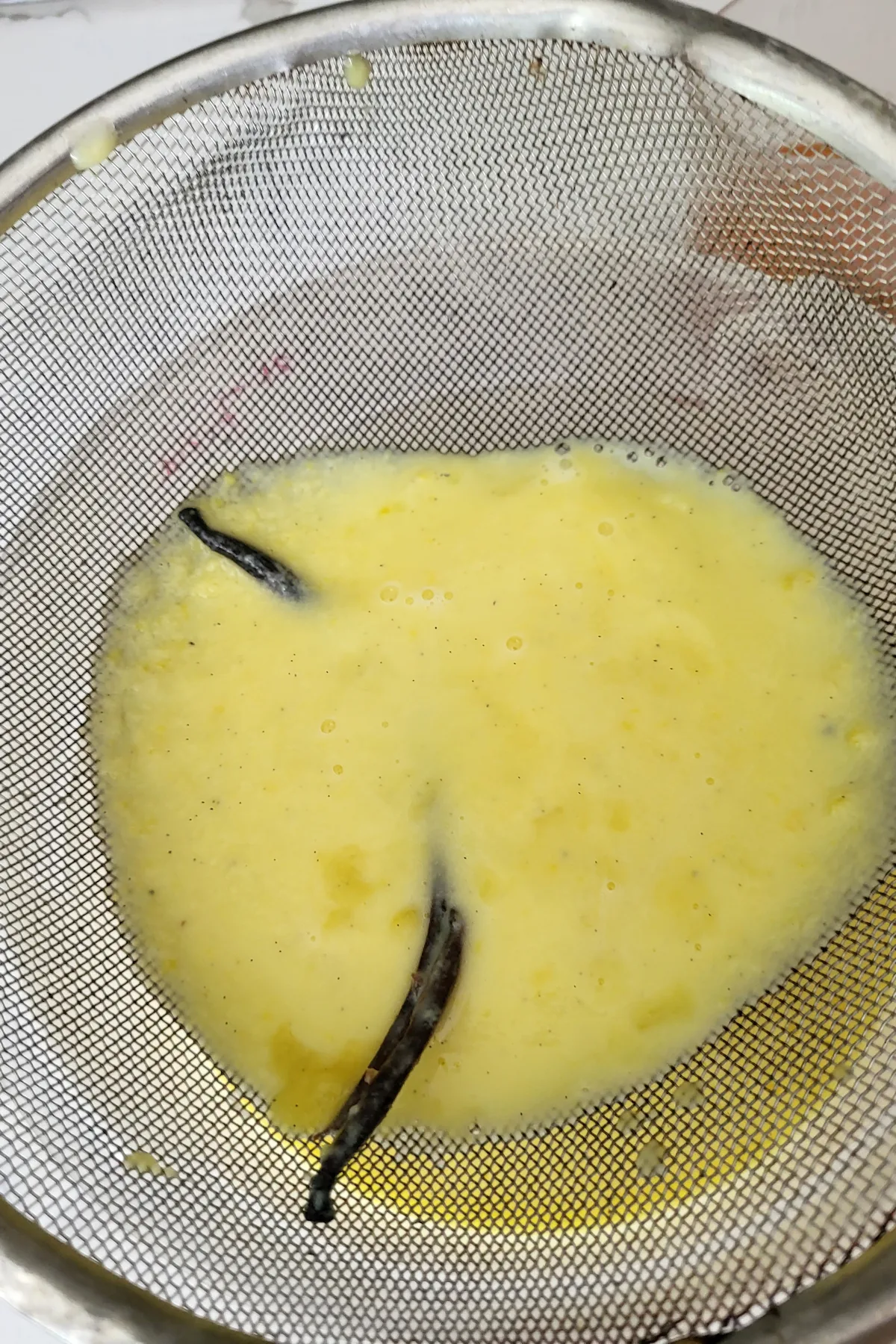 a strainer filled with custard and a vanilla bean.