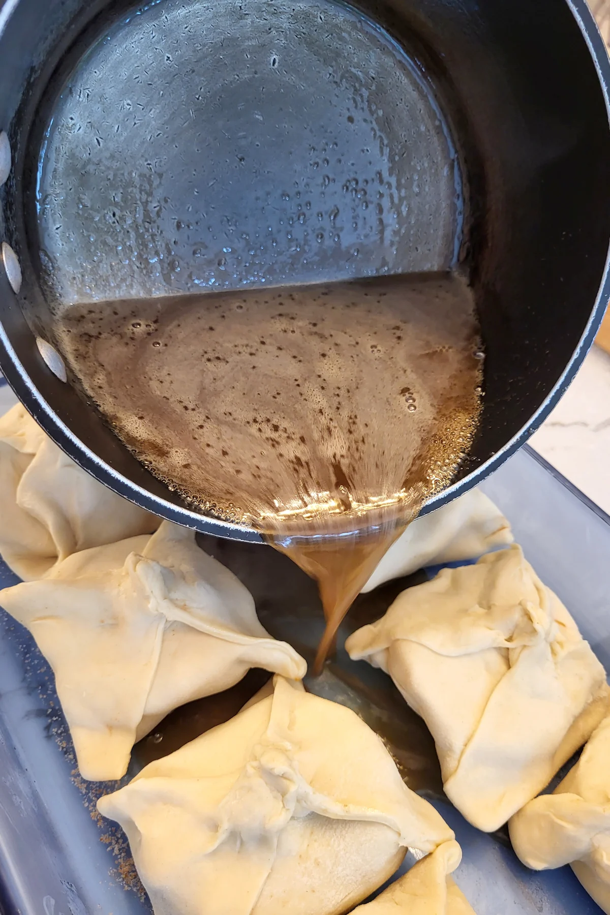 Syrup being poured from a pot  between dumplings in a pan.
