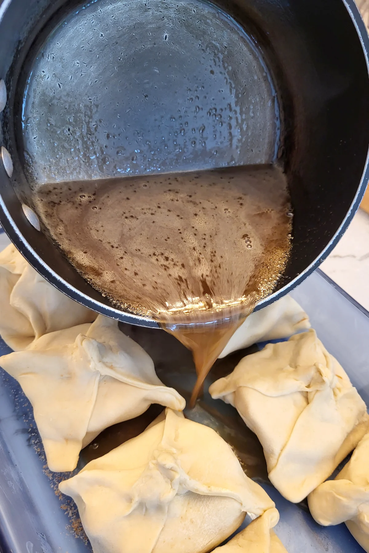 Syrup being poured from a pot between dumplings in a pan.