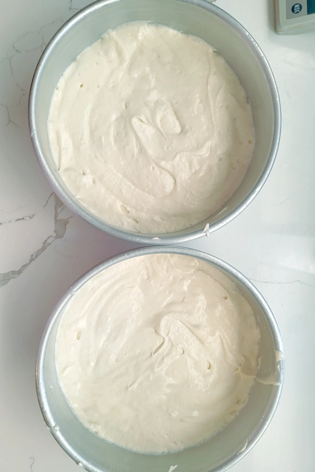 two cakes pans filled with white cake batter.