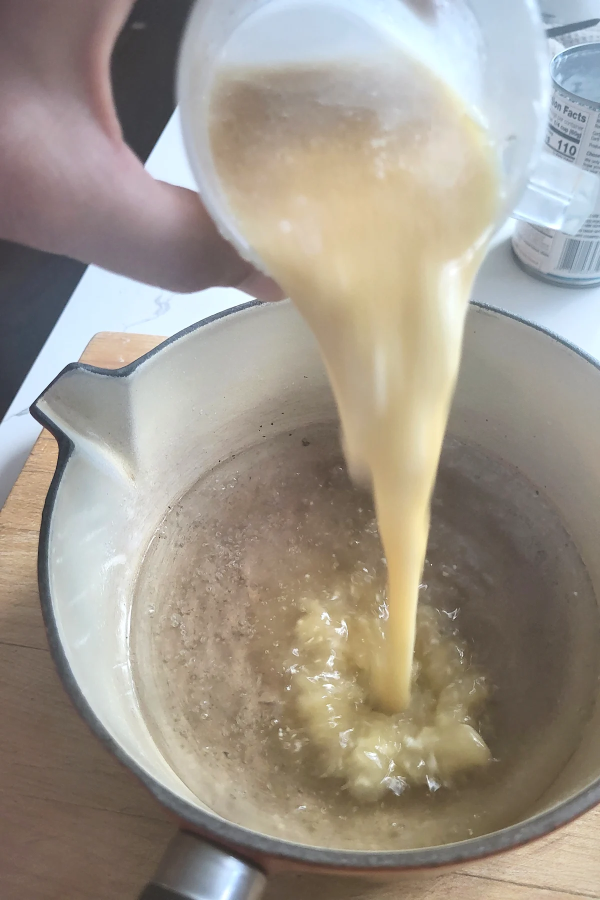 pouring coconut milk into a pot of sugar syrup.