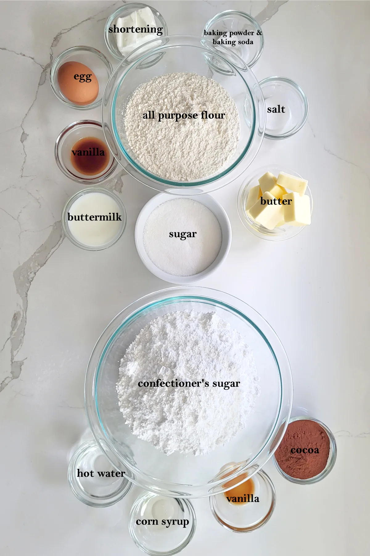 bowls of ingredients for black and white cookies on a white surface.