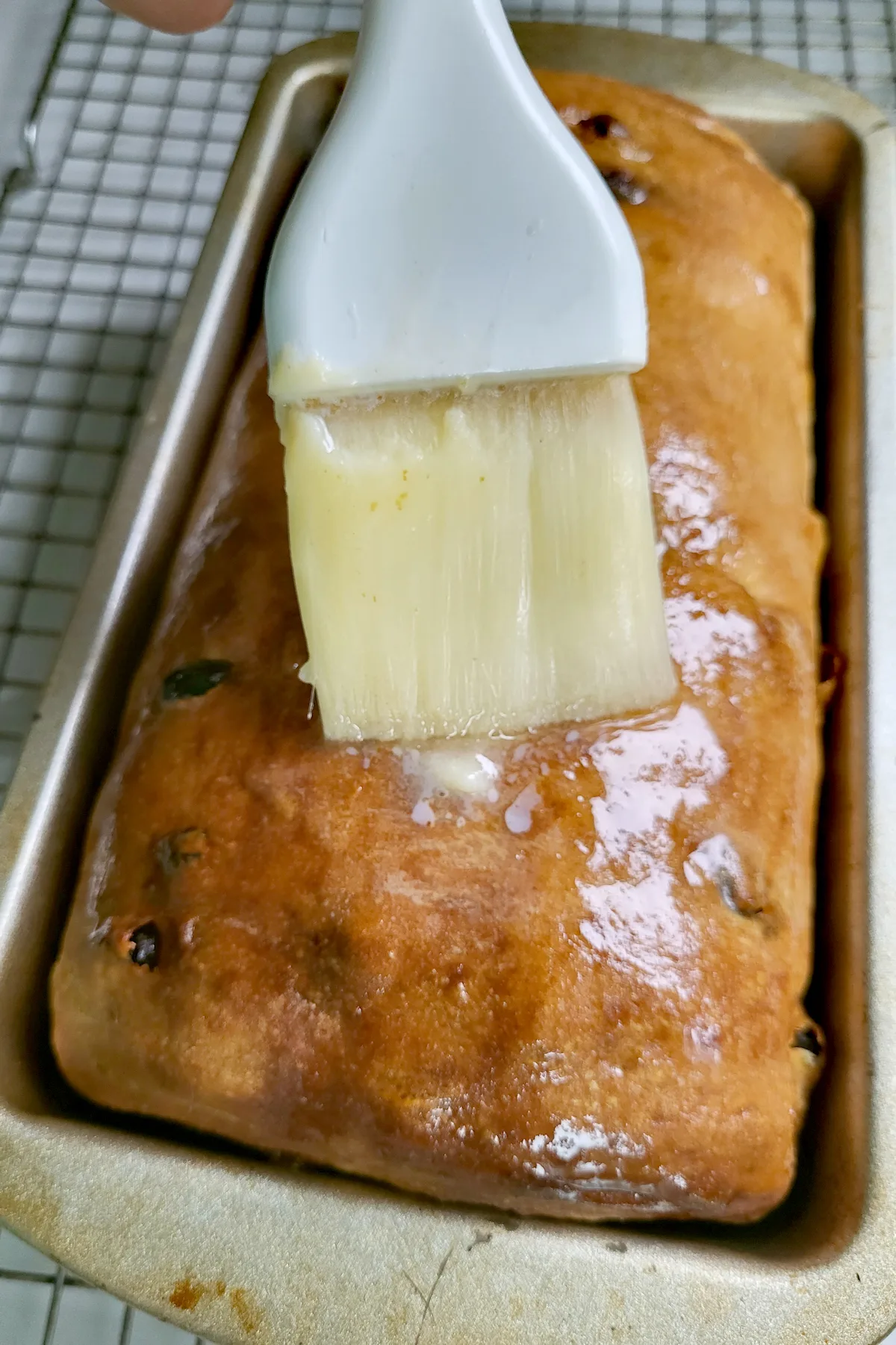 A loaf of bread in a pan being brushed with melted butter.