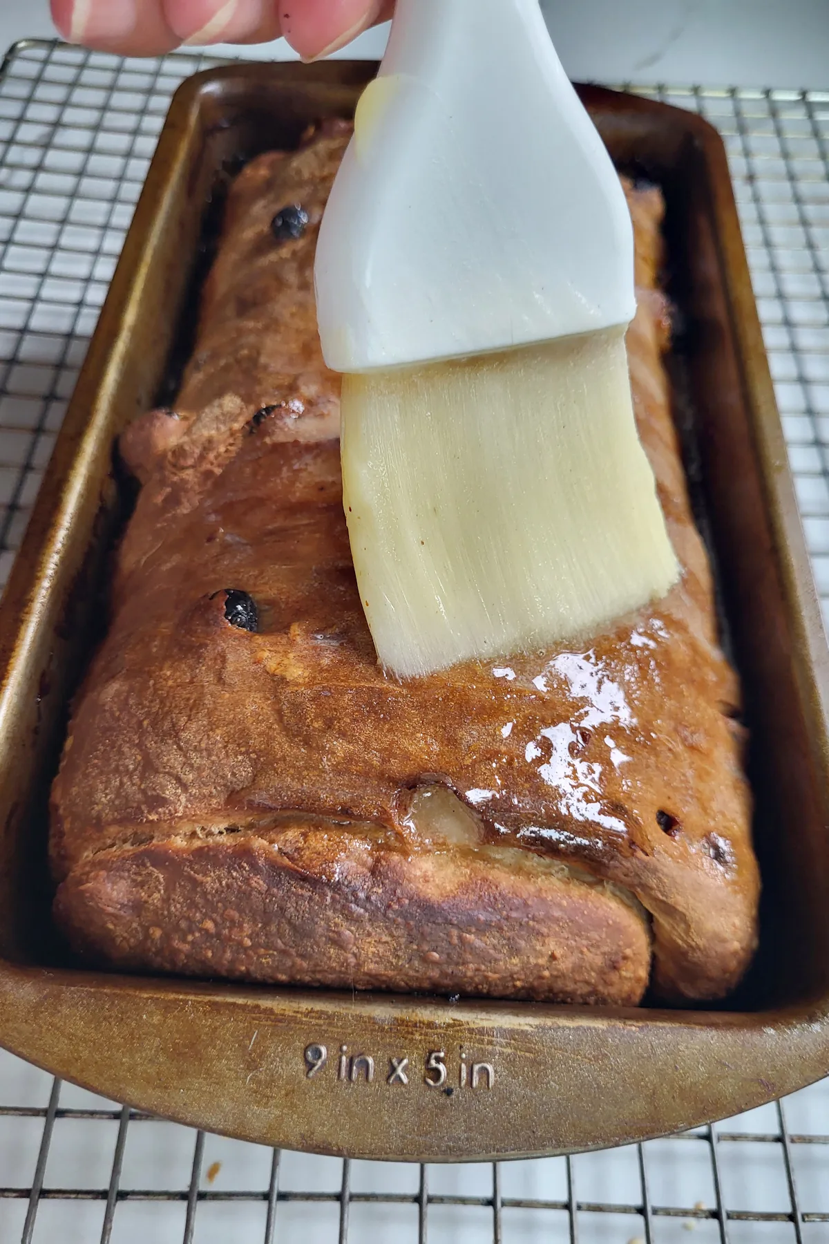 Brushing melted butter onto raisin bread in a pan.