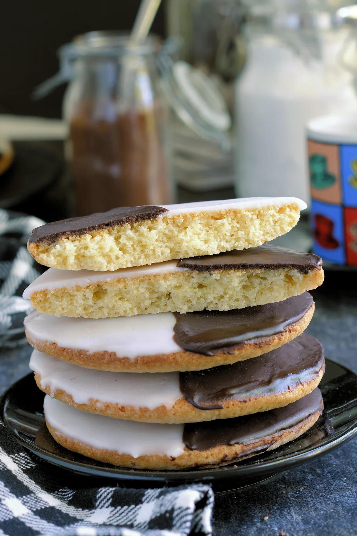 a stack of black and white cookies on a black plate. One cookie is broken in half.
