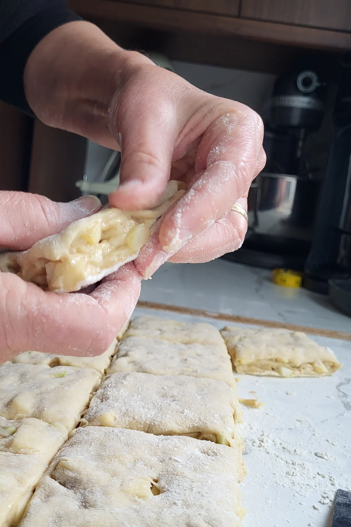 a hand pinching apples into dough