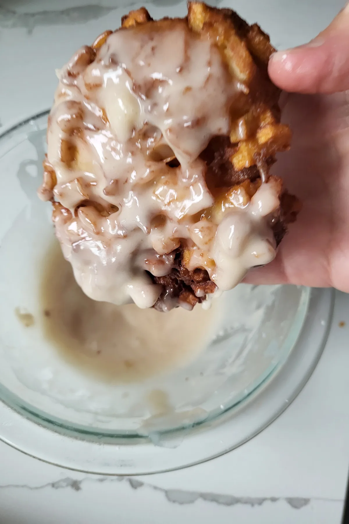 a hand holding a large apple fritter