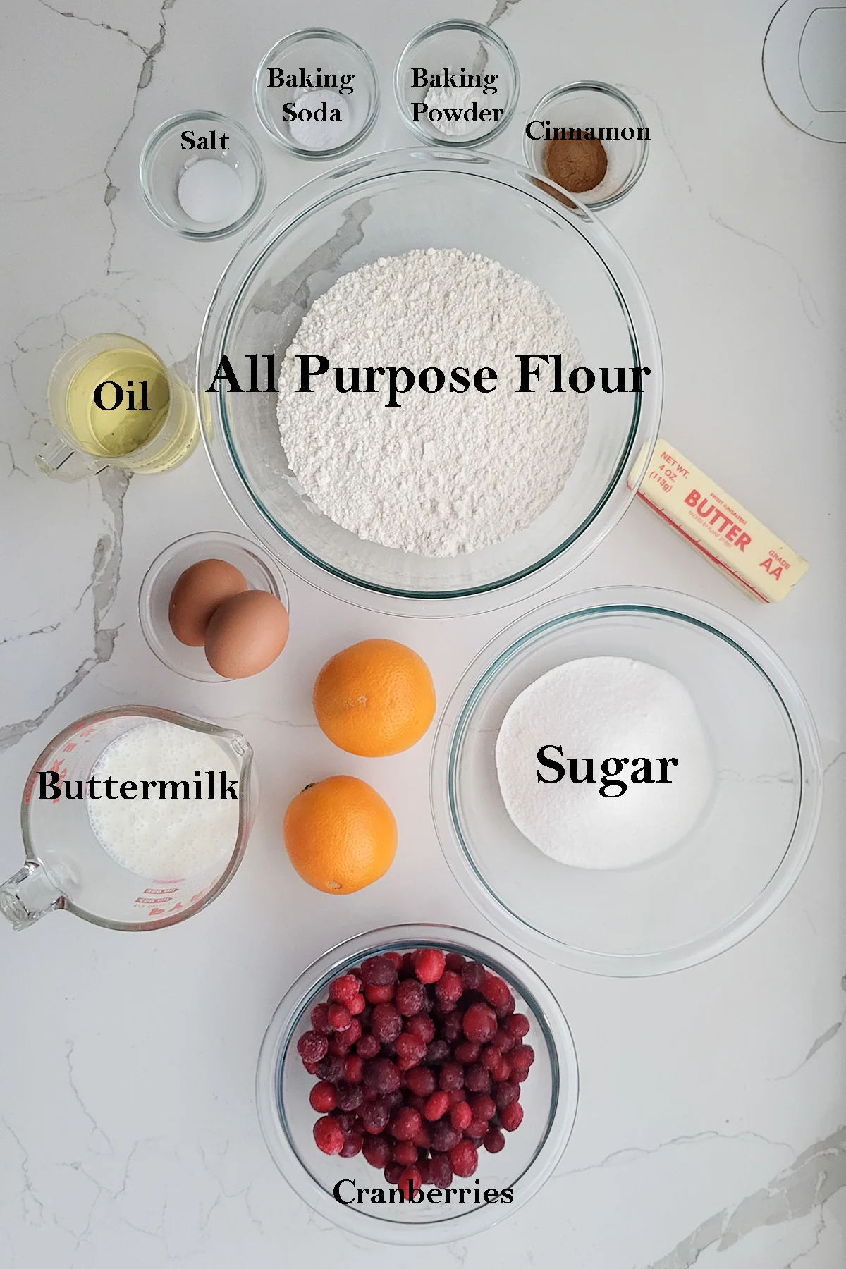 bowls of ingredients for making cranberry muffins on a white surface.