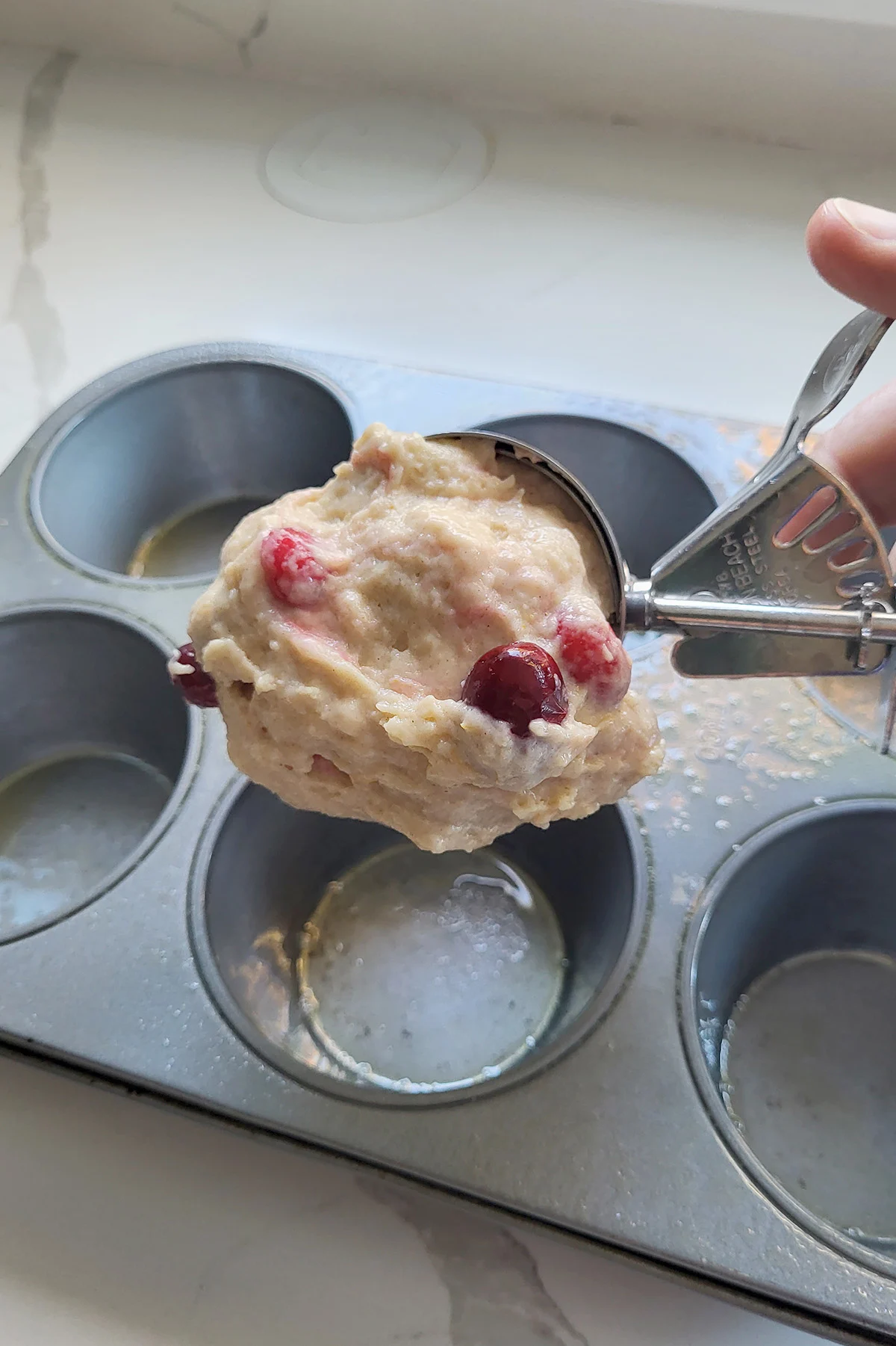A scooper putting batter into a muffin tin.