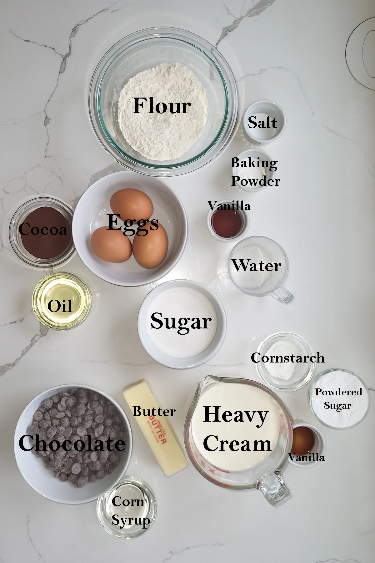 ingredients for chocolate swiss roll cake in bowls on a marble surface.