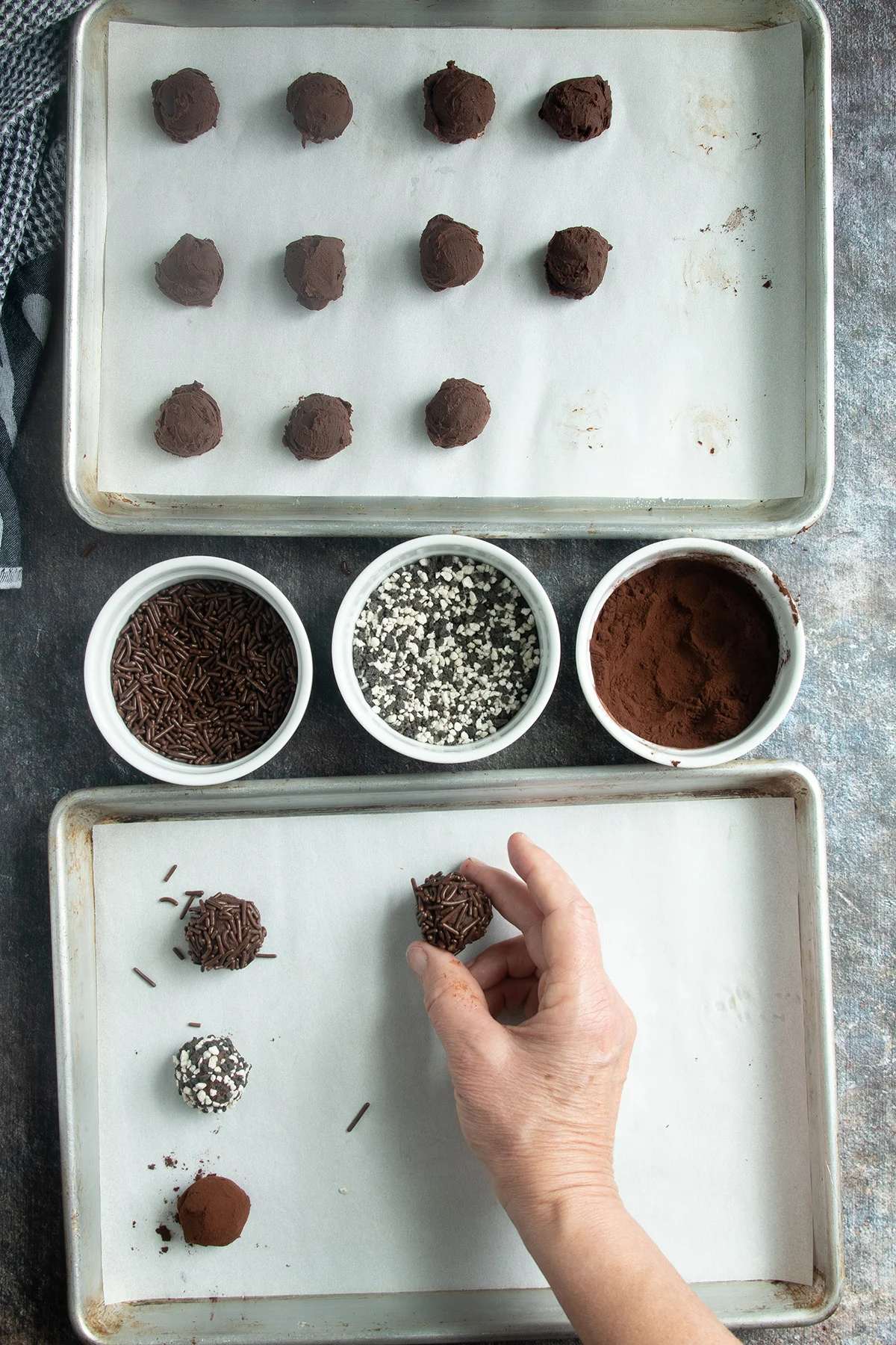 a tray of truffles, three bowls of sprinkles a hand rolling a truffle in sprinkles