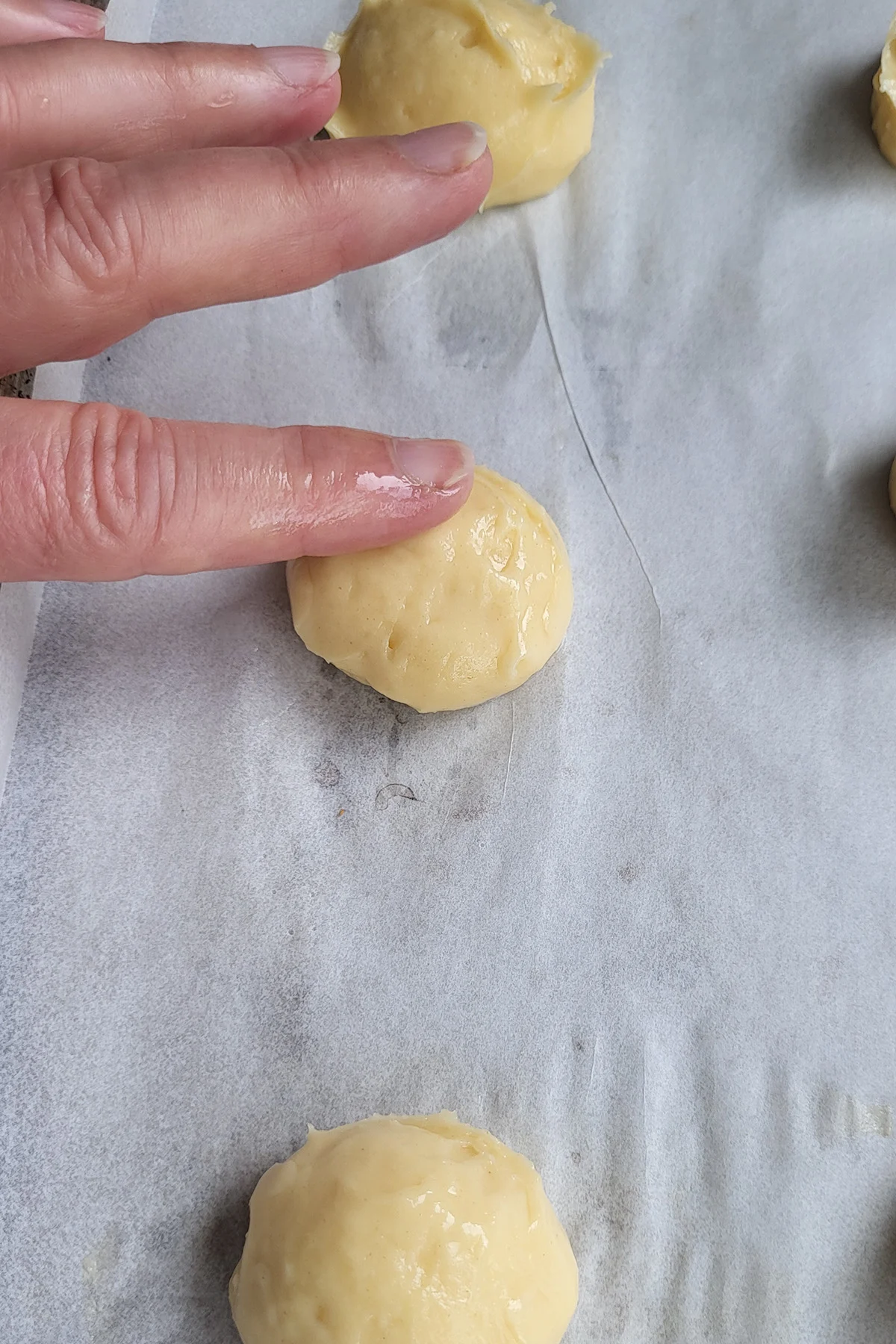a finger smoothing the top of an unbaked cream puff.