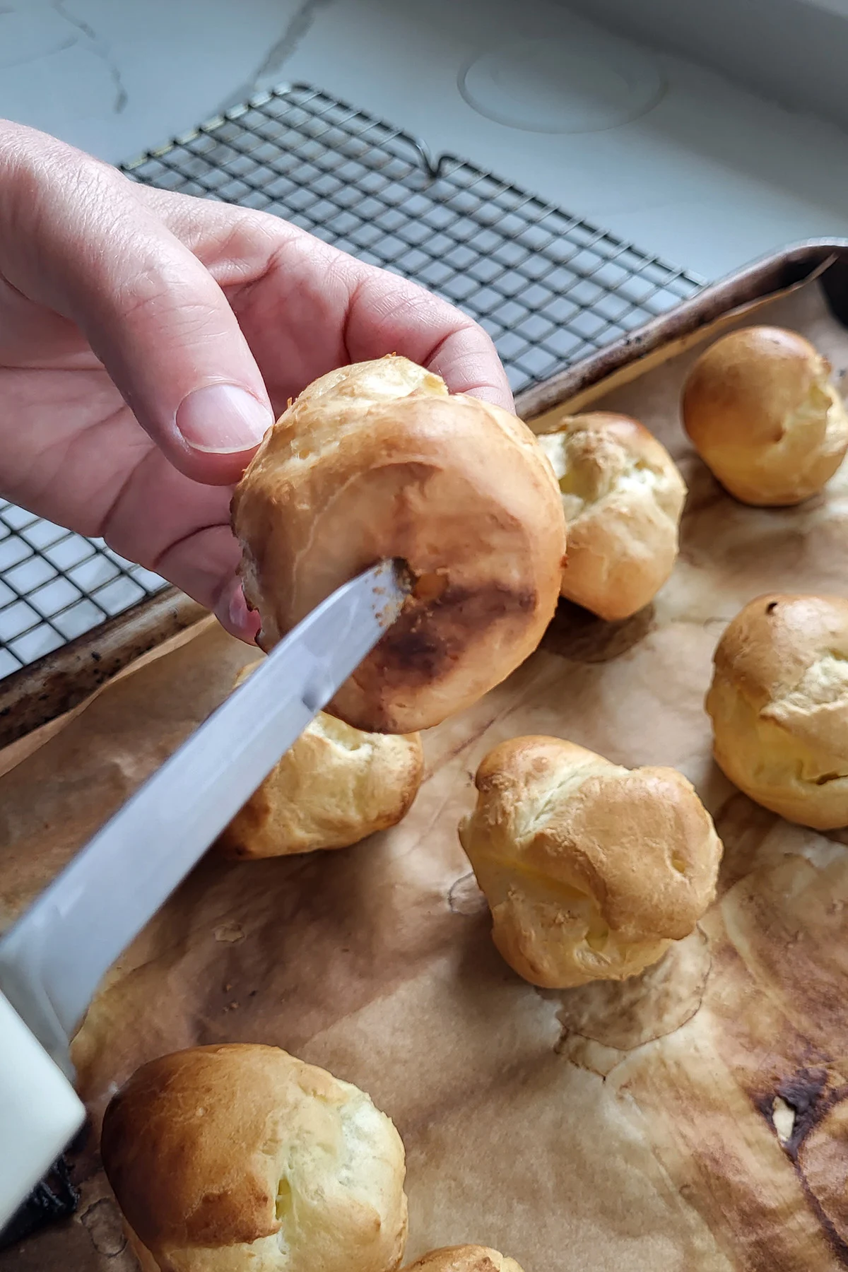 a paring knife poking a hole in the bottom of a cream puff.