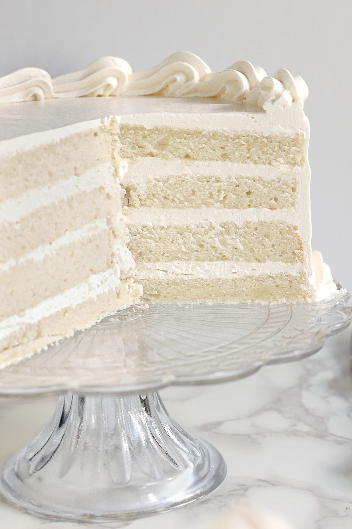 An cross section of a four layer velvety soft white cake 1/2 on a glass cake stand.