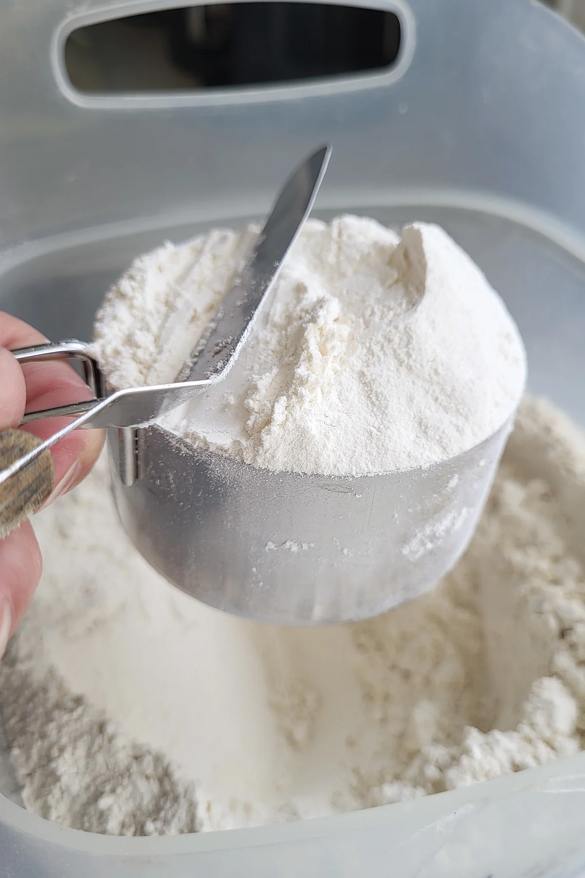 a cup of flour with a spatula sweeping away excess.