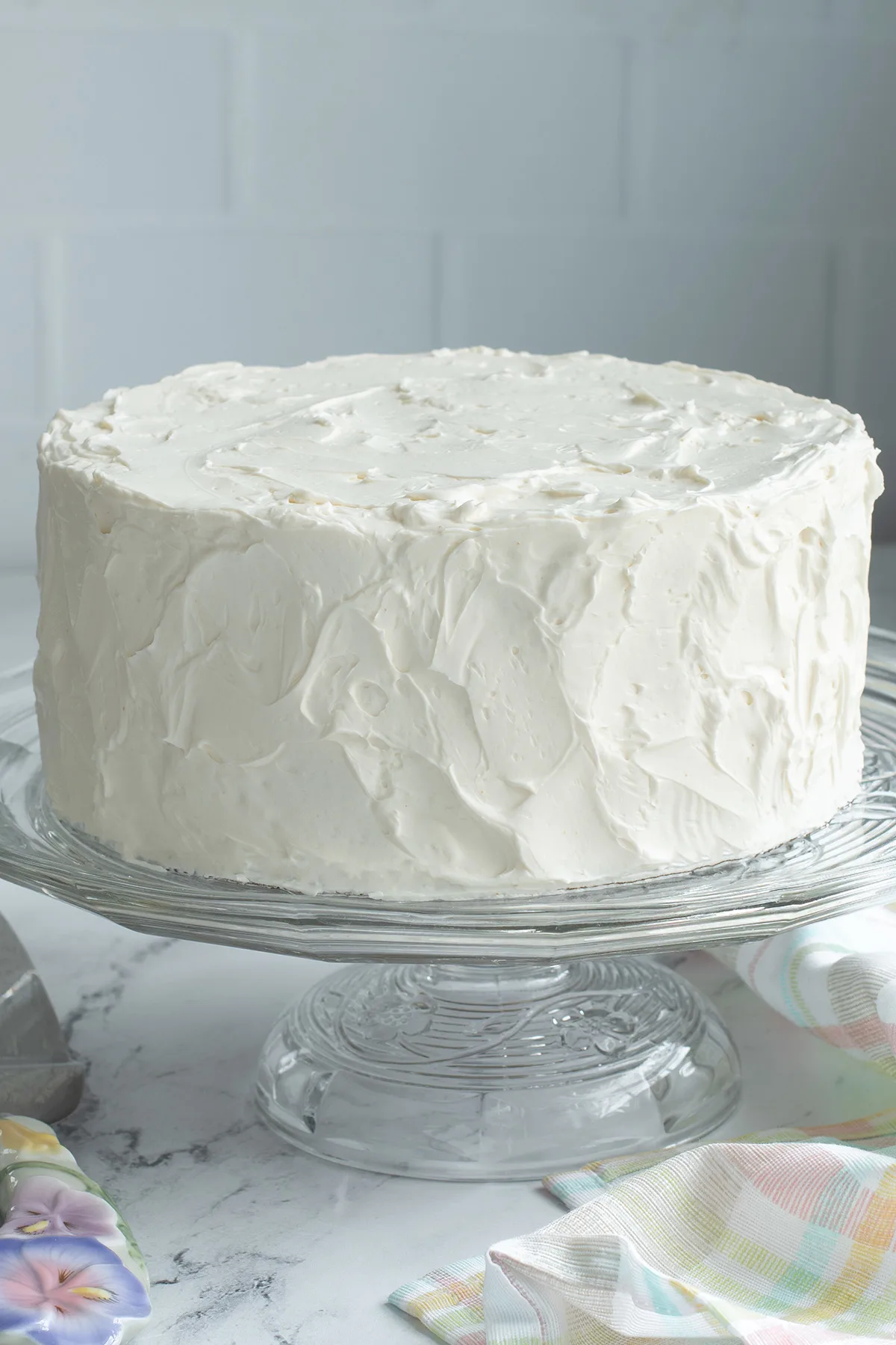 a vanilla frosted cake on a glass cake stand.