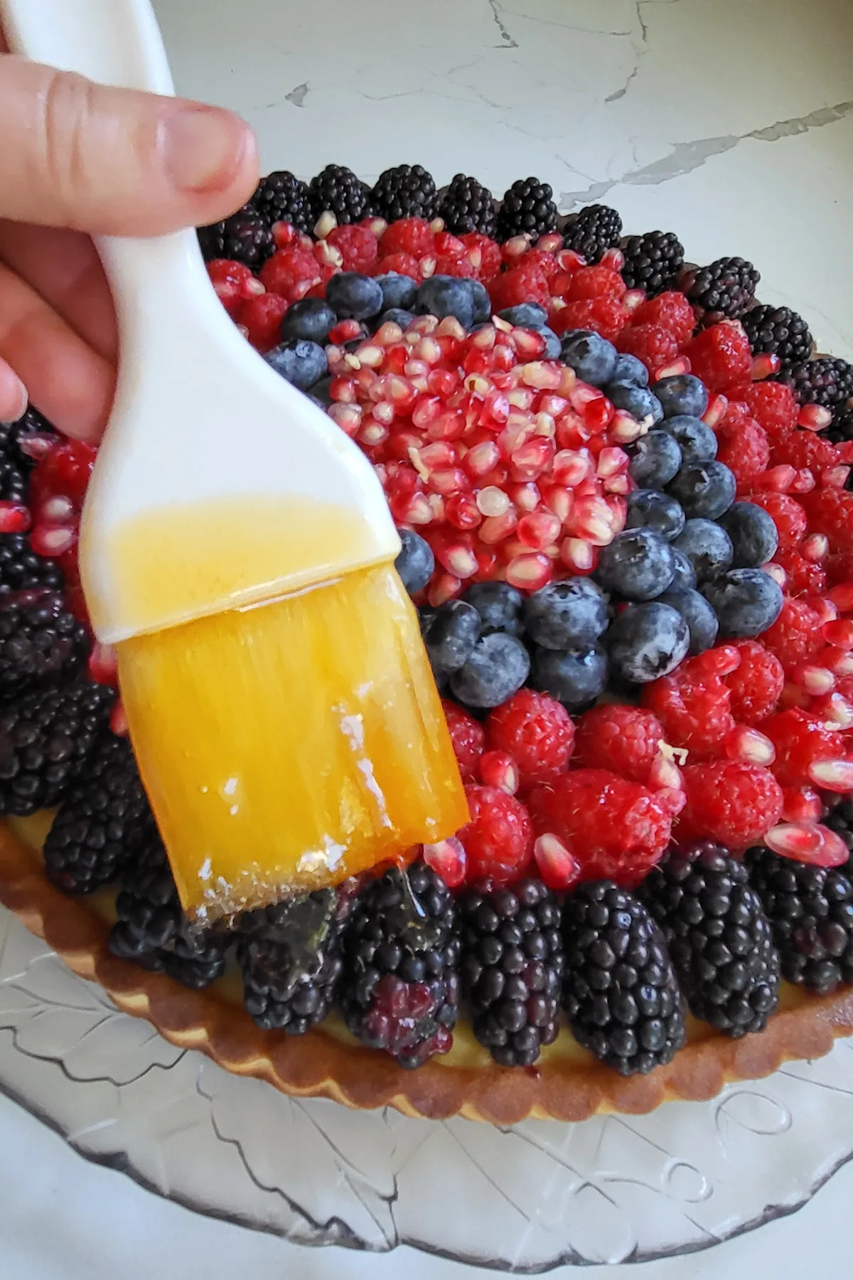 A fruit tart being brushed with melted apricot preserves.