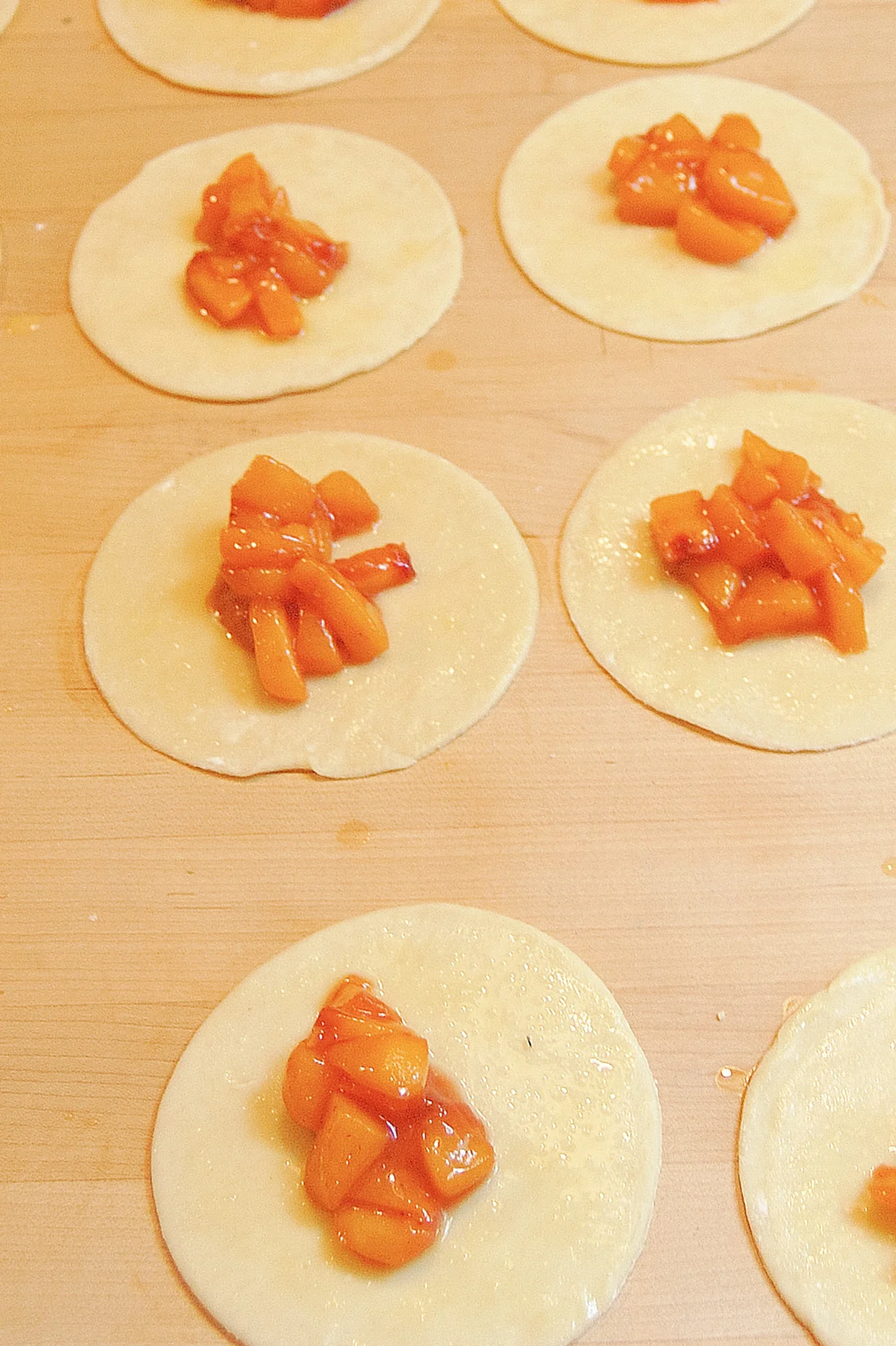 Round of pie dough with dollops of peach filling on a wood surface.