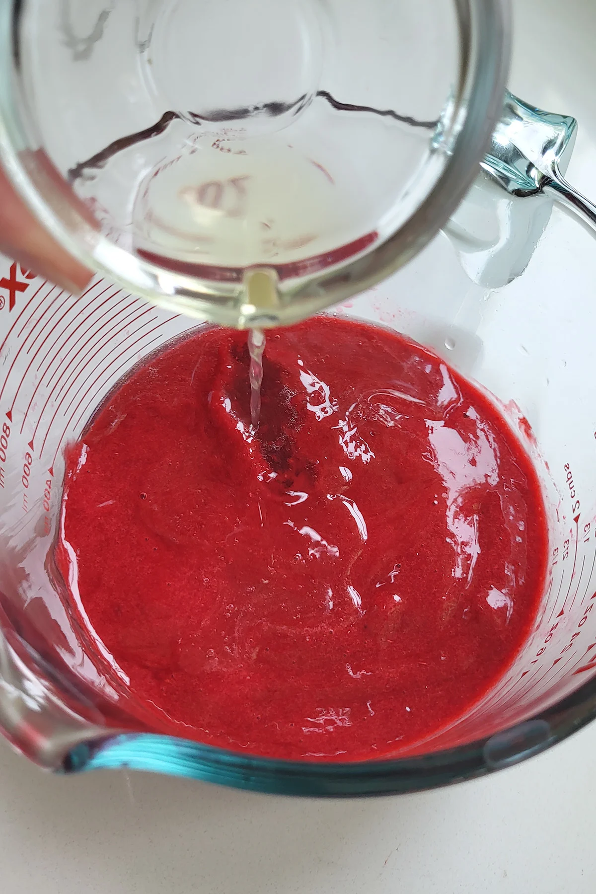 Limoncello pouring into a cup of raspberry puree.