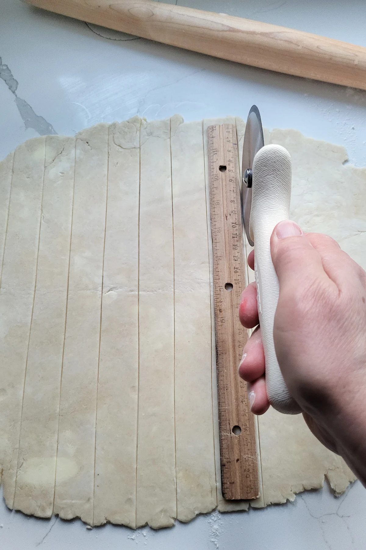Rolled pie dough being cut into strips with a pizza cutter.