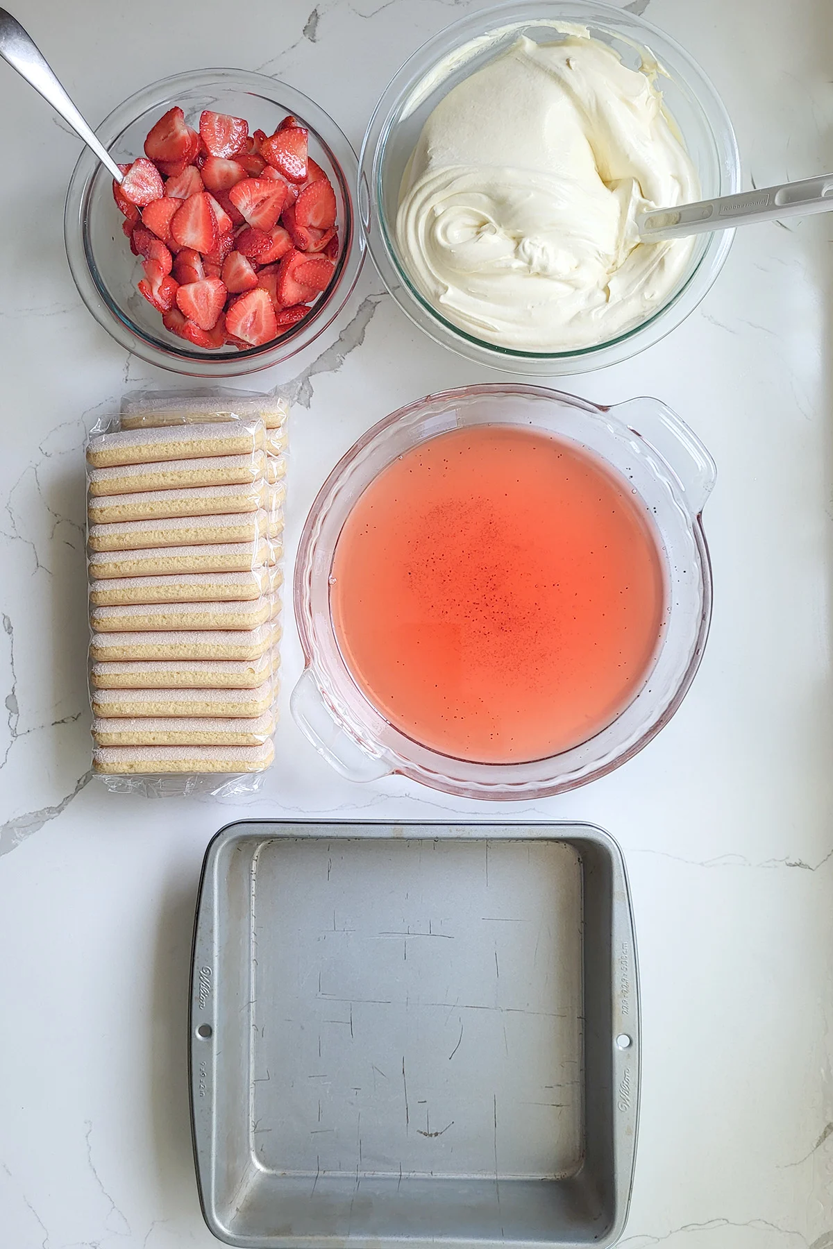 A square pan, a package of cookies, a bowl of syrup, a bowl of cream and a bowl of strawberries.