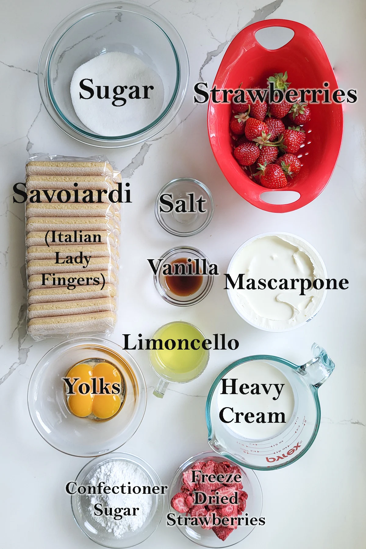 Ingredients for strawberry tiramisu arrange in bowls on a white countertop.