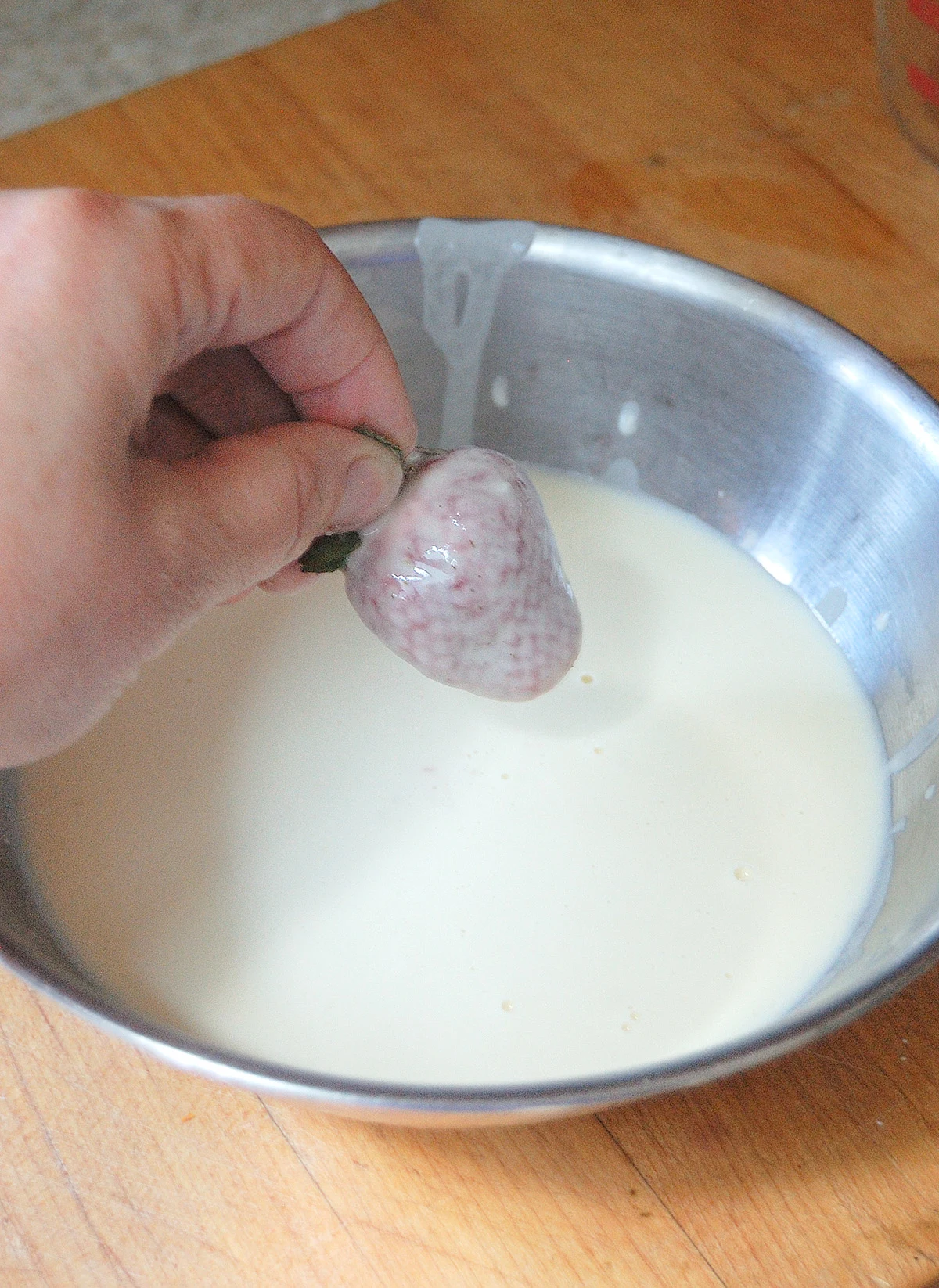 A hand dipping a strawberry into batter.