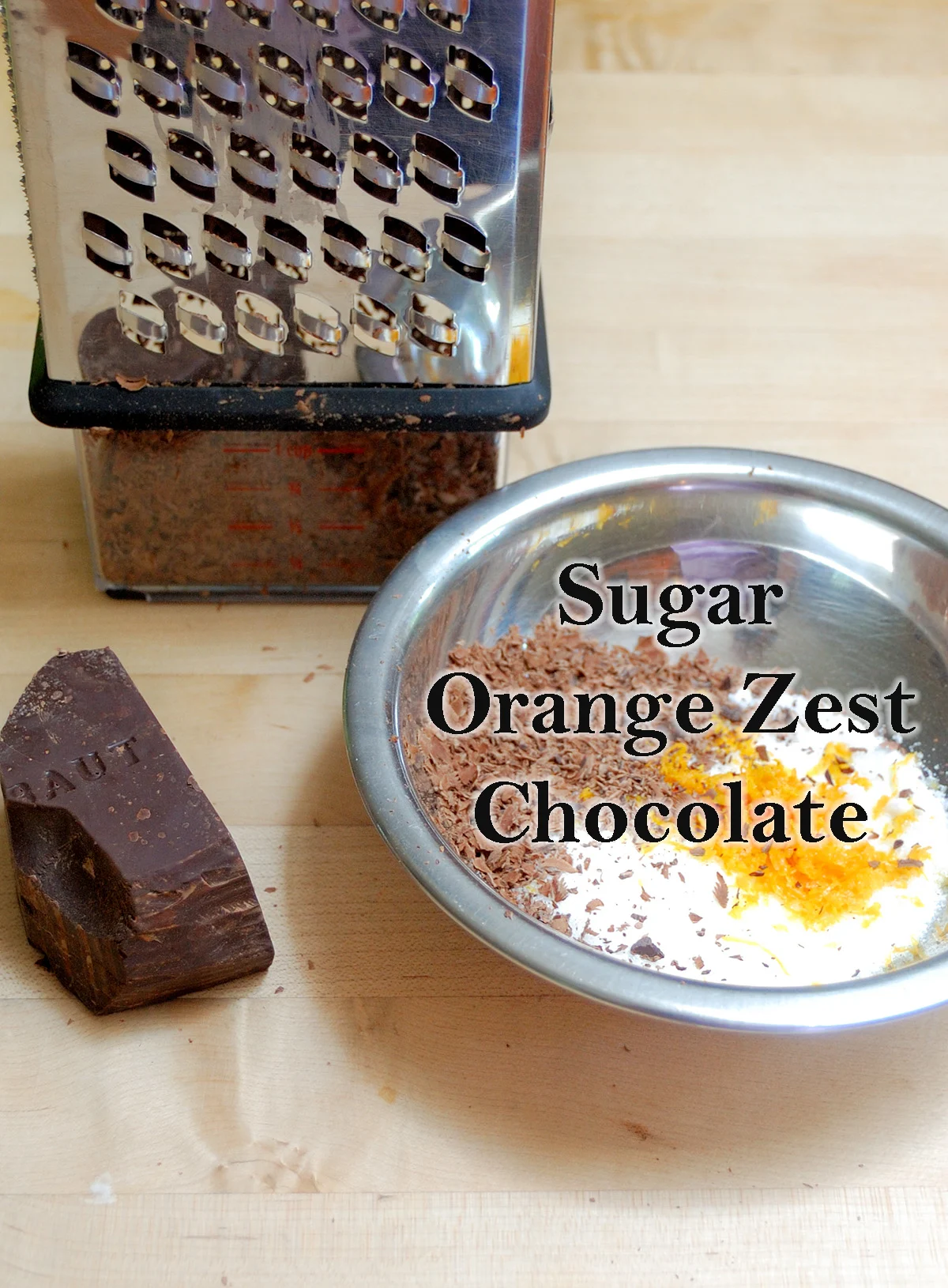 A grater, a piece of chocolate and a bowl with sugar, orange zest and chocolate.