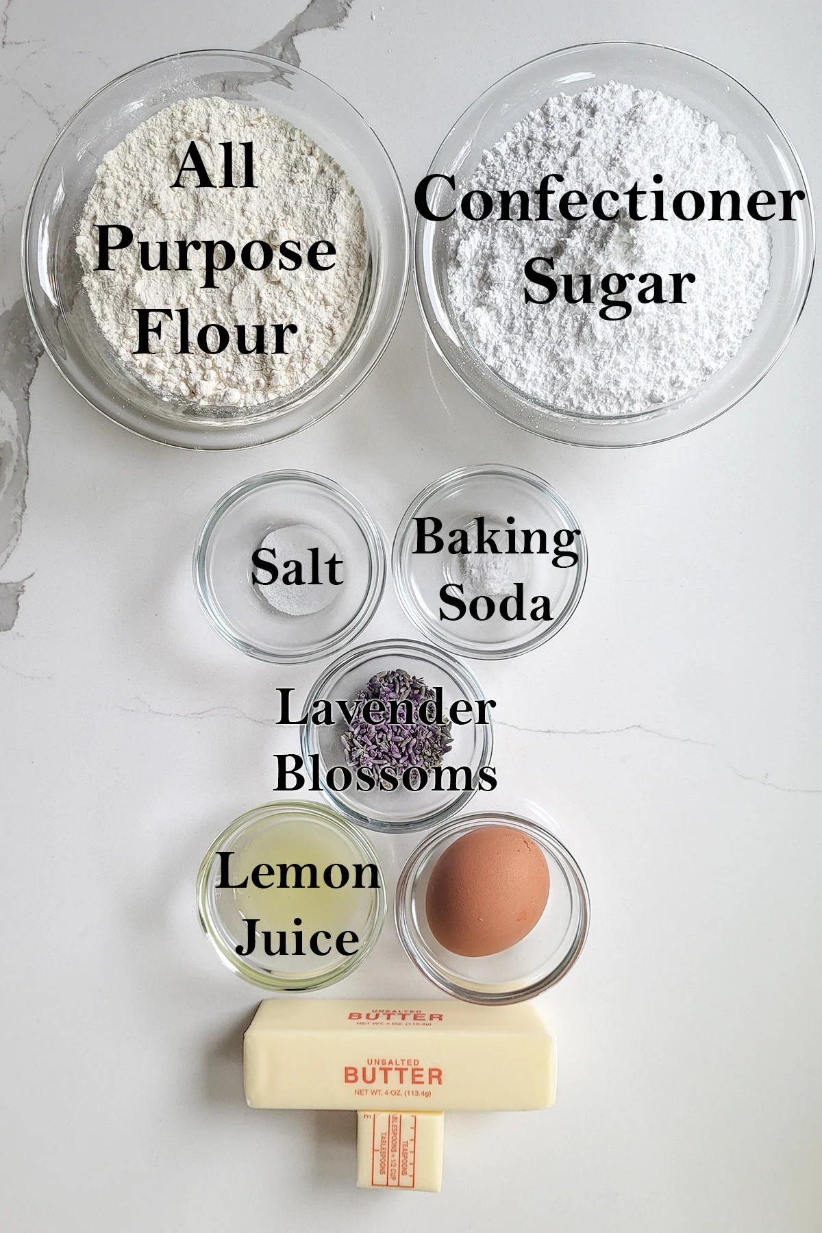 Ingredients for lavender cookies in bowls on a white surface.