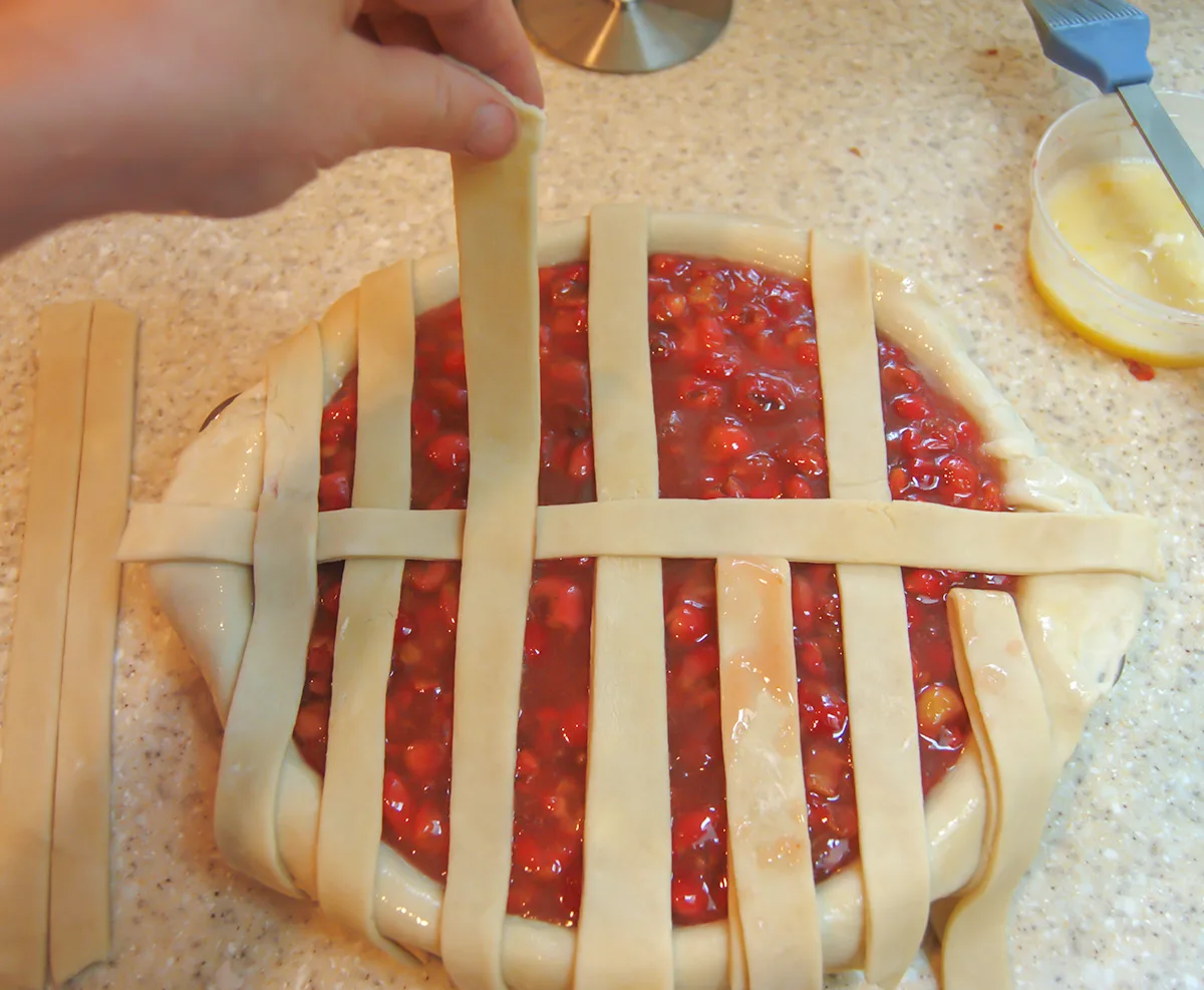 Weaving dough strips over cherry pie filling.
