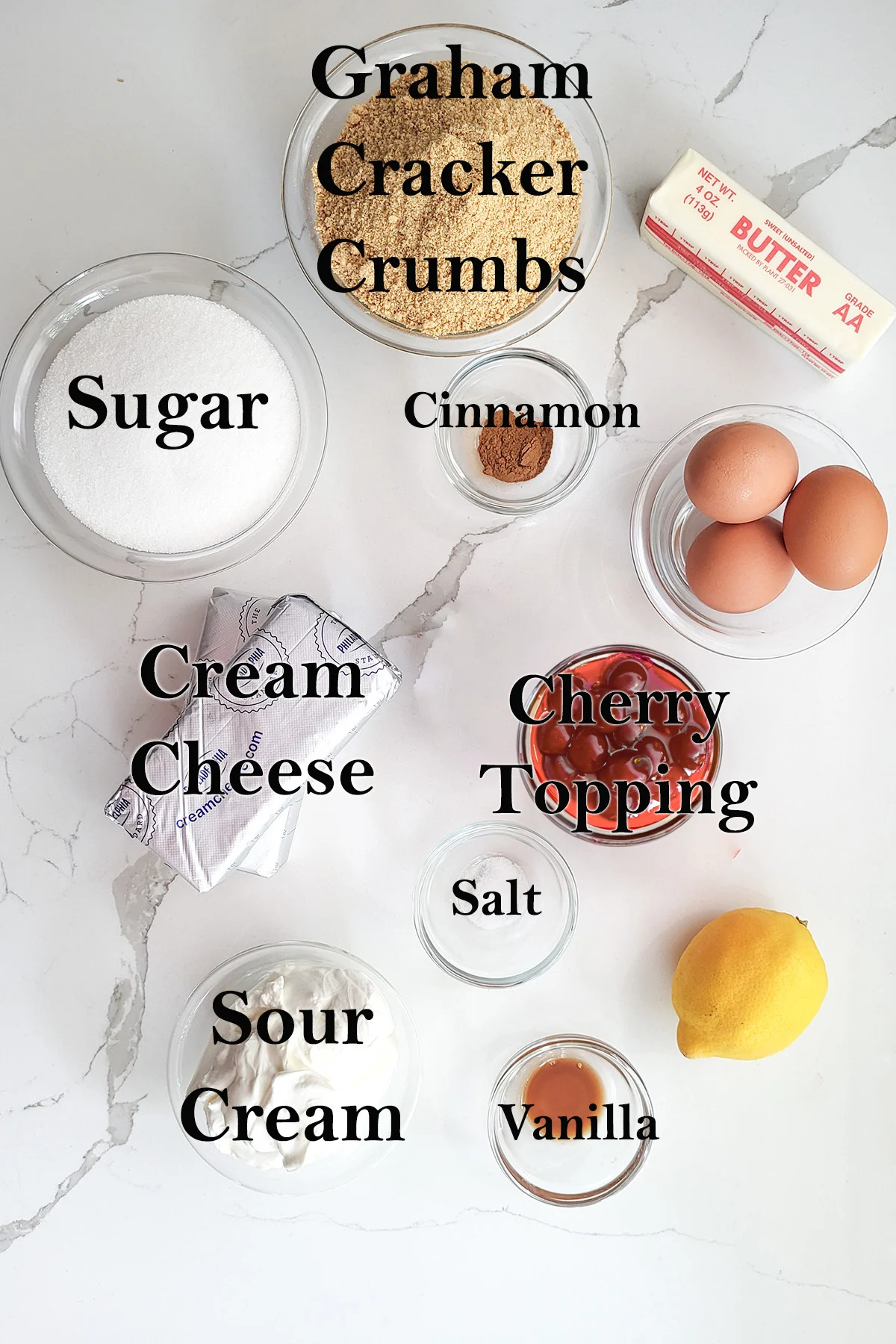 ingredients for new york cheesecake in glass bowls on a white surface.