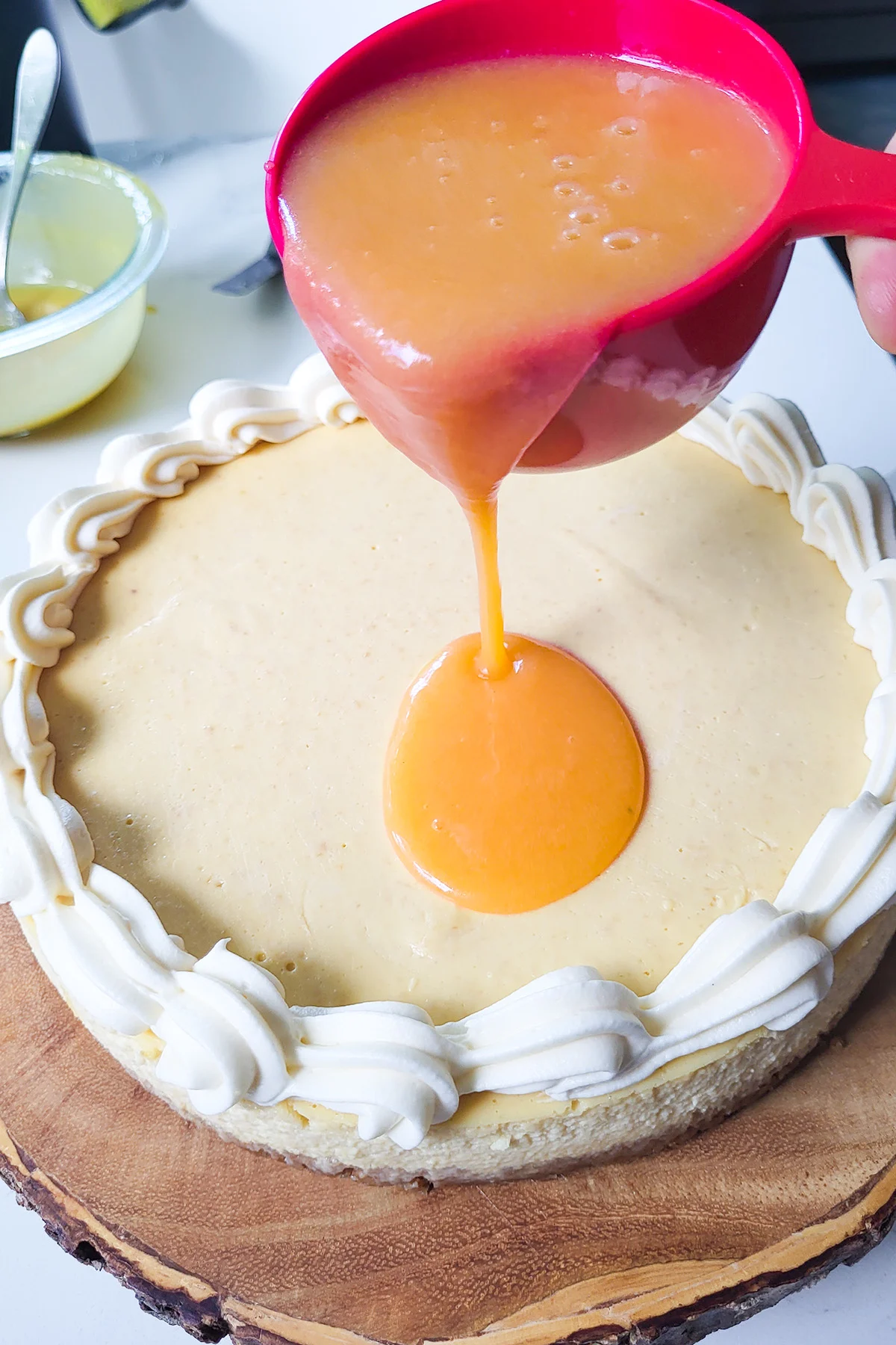 A cup of peach glaze pouring onto a cheesecake with frosting border.