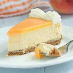 a slice of peach cheesecake on a white plate with a fork.