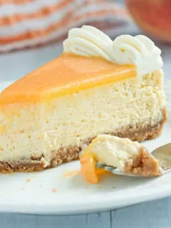 a slice of peach cheesecake on a white plate with a fork.