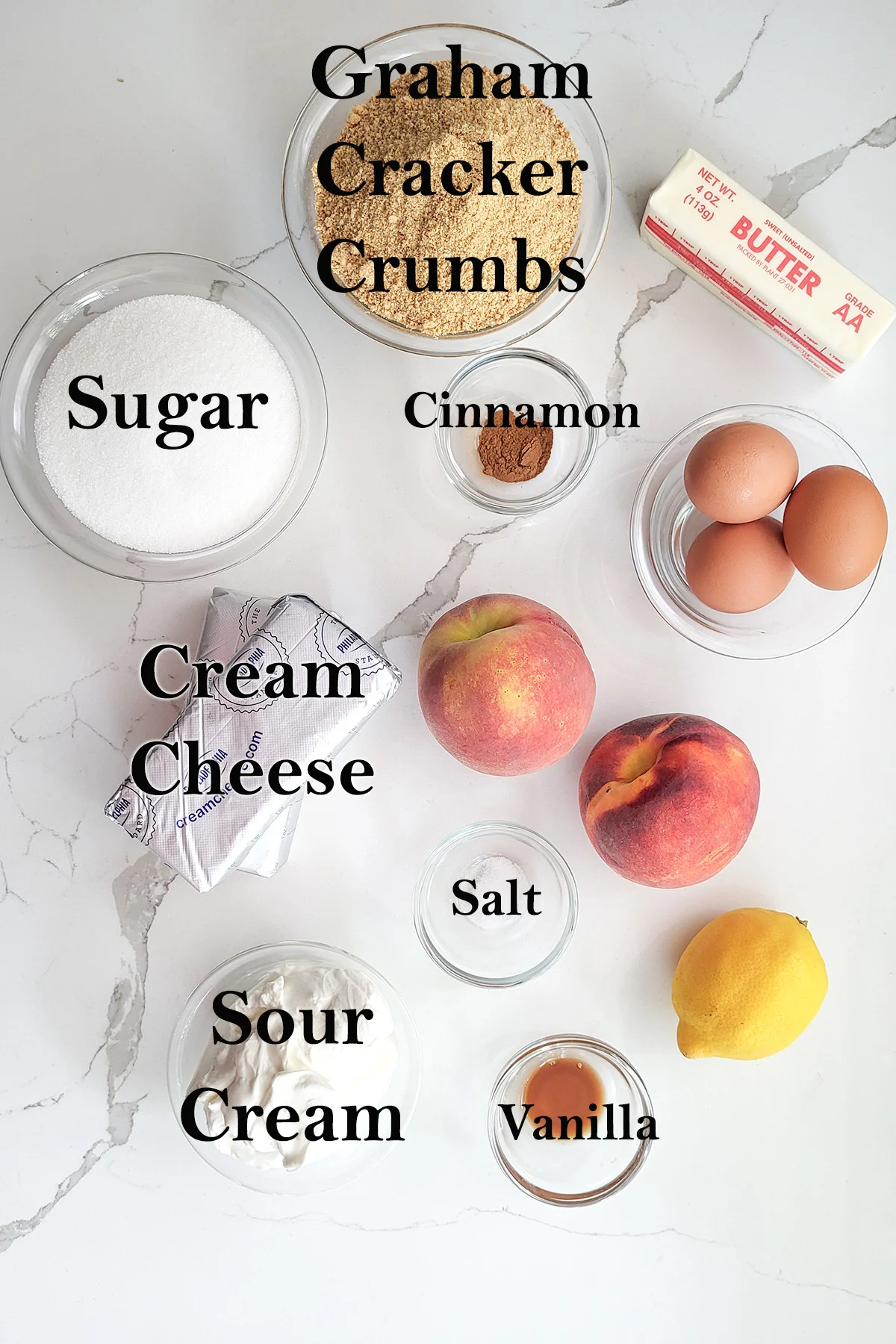 INGREDIENTS for making peach cheesecake in glass bowls on a white surface.