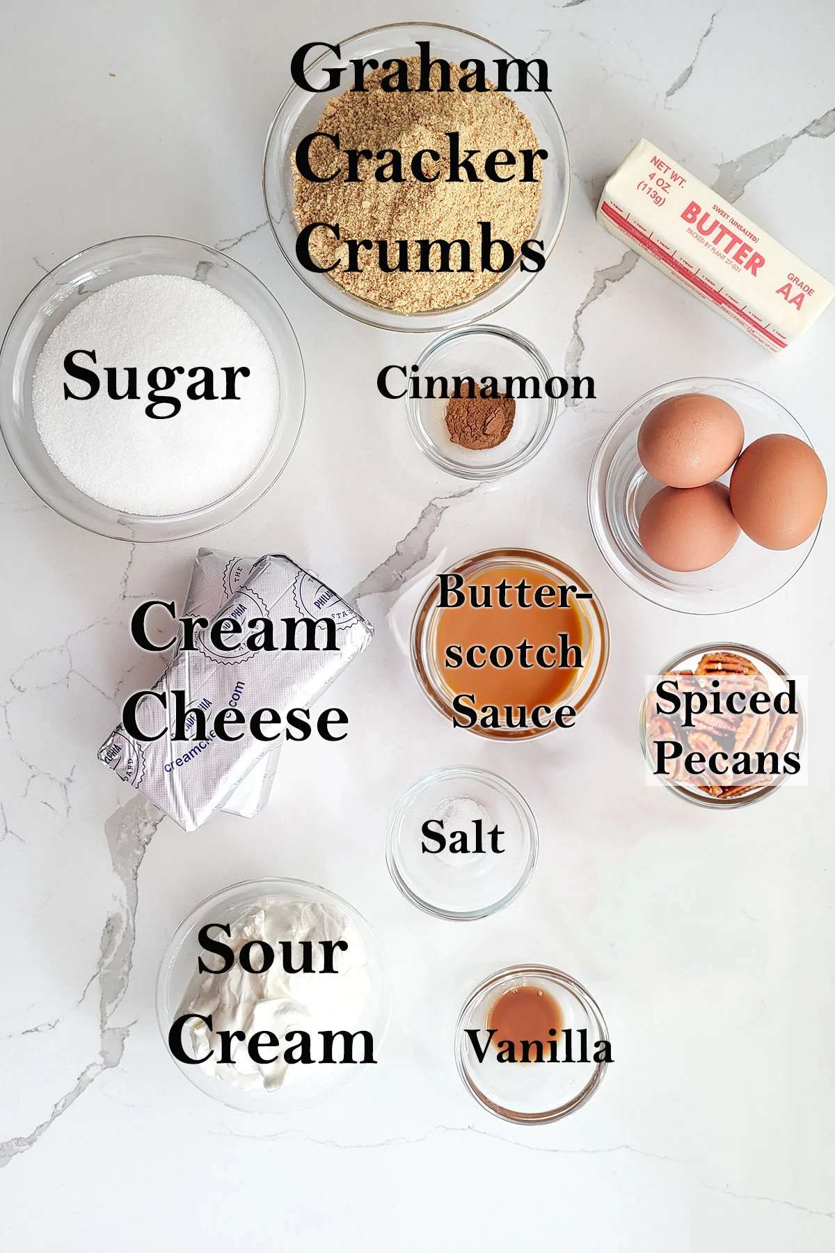 ingredients for butterscotch cheesecake in glass bowls on a white surface.