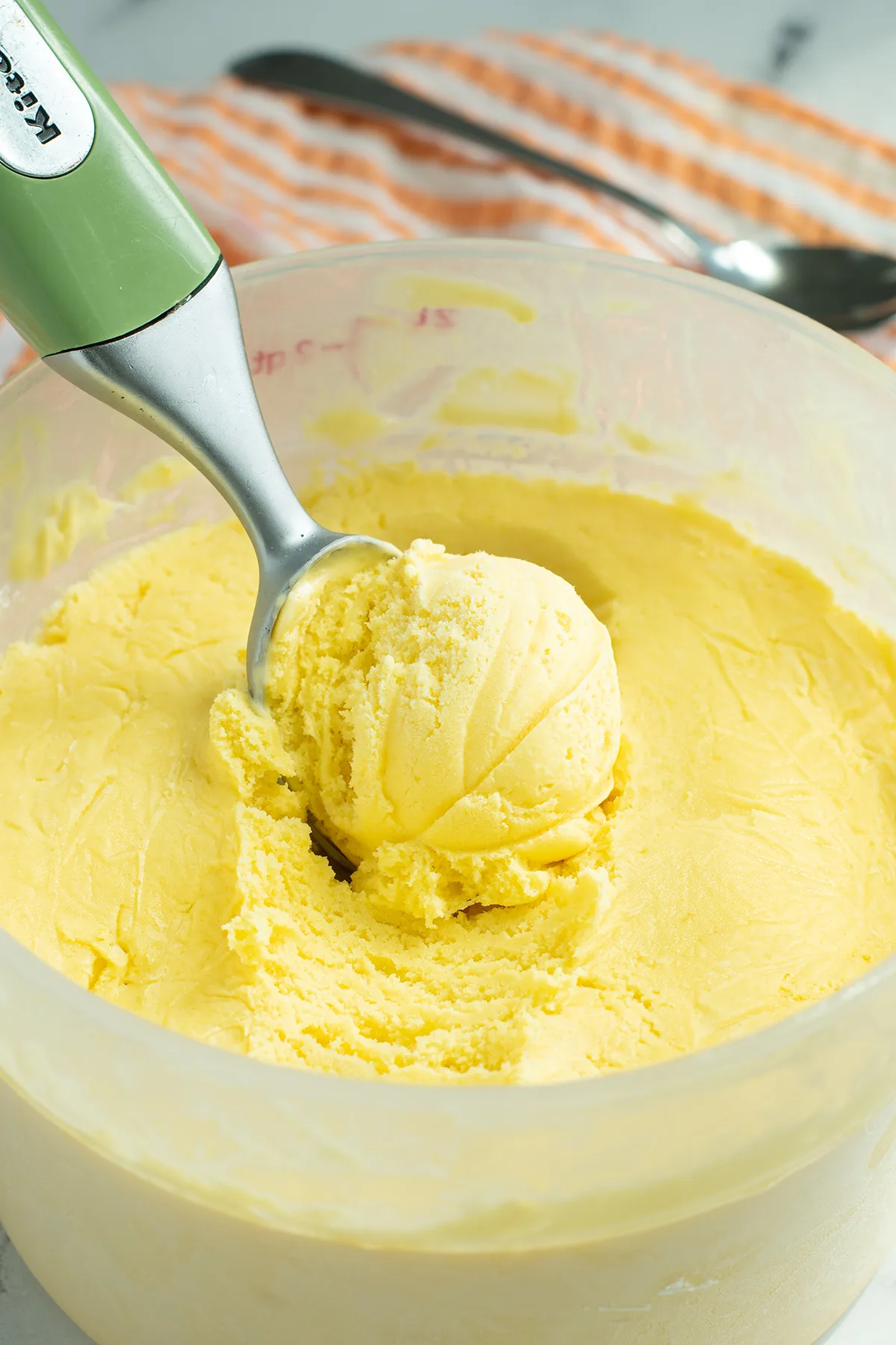 a tub of mango ice cream with a scooper in it.