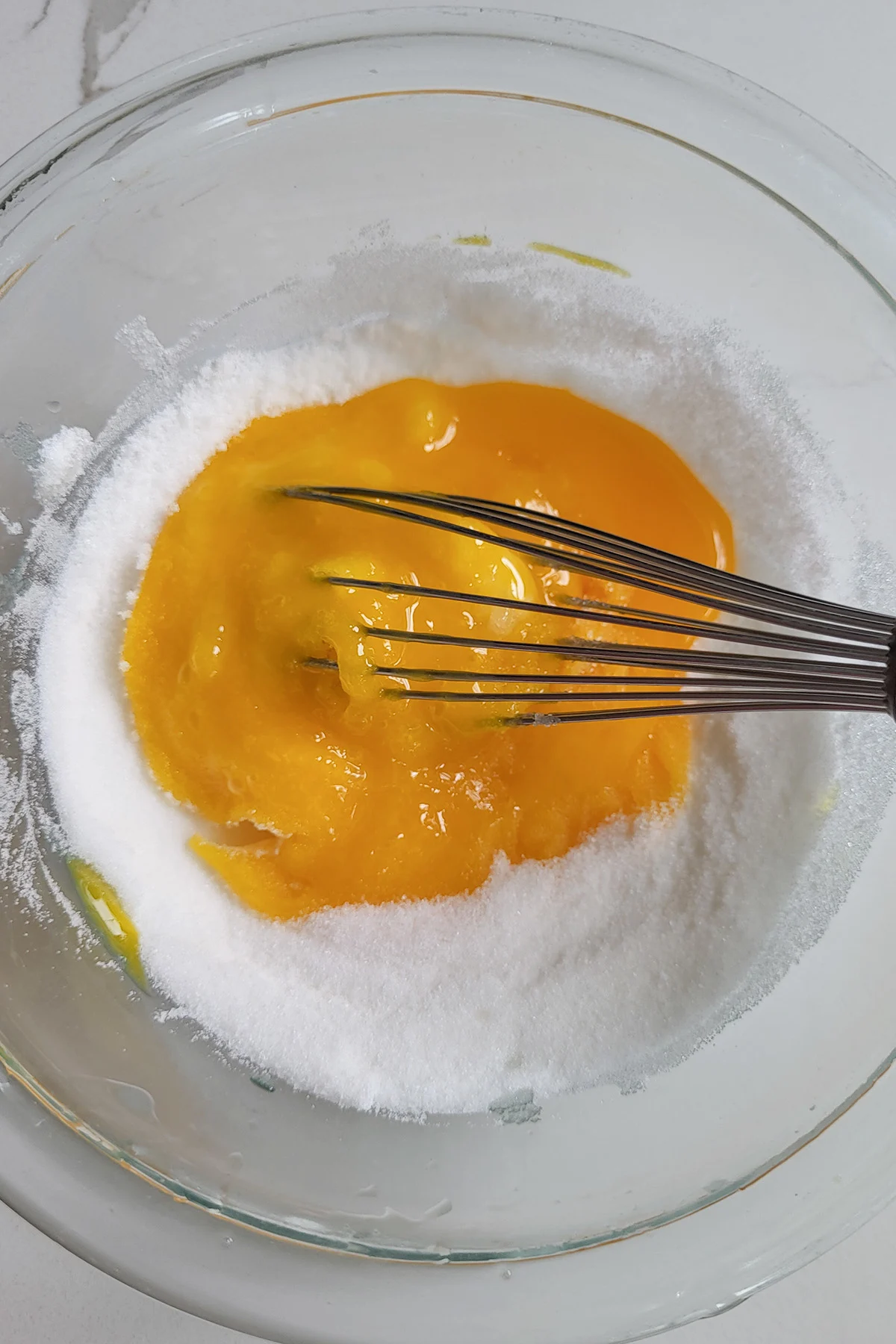 a bowl of egg yolks and sugar with a whisk.