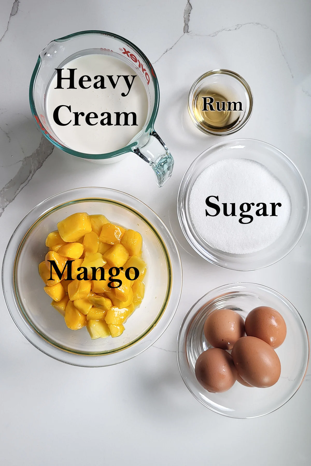 ingredients for mango ice cream in glass bowls on a white surface.