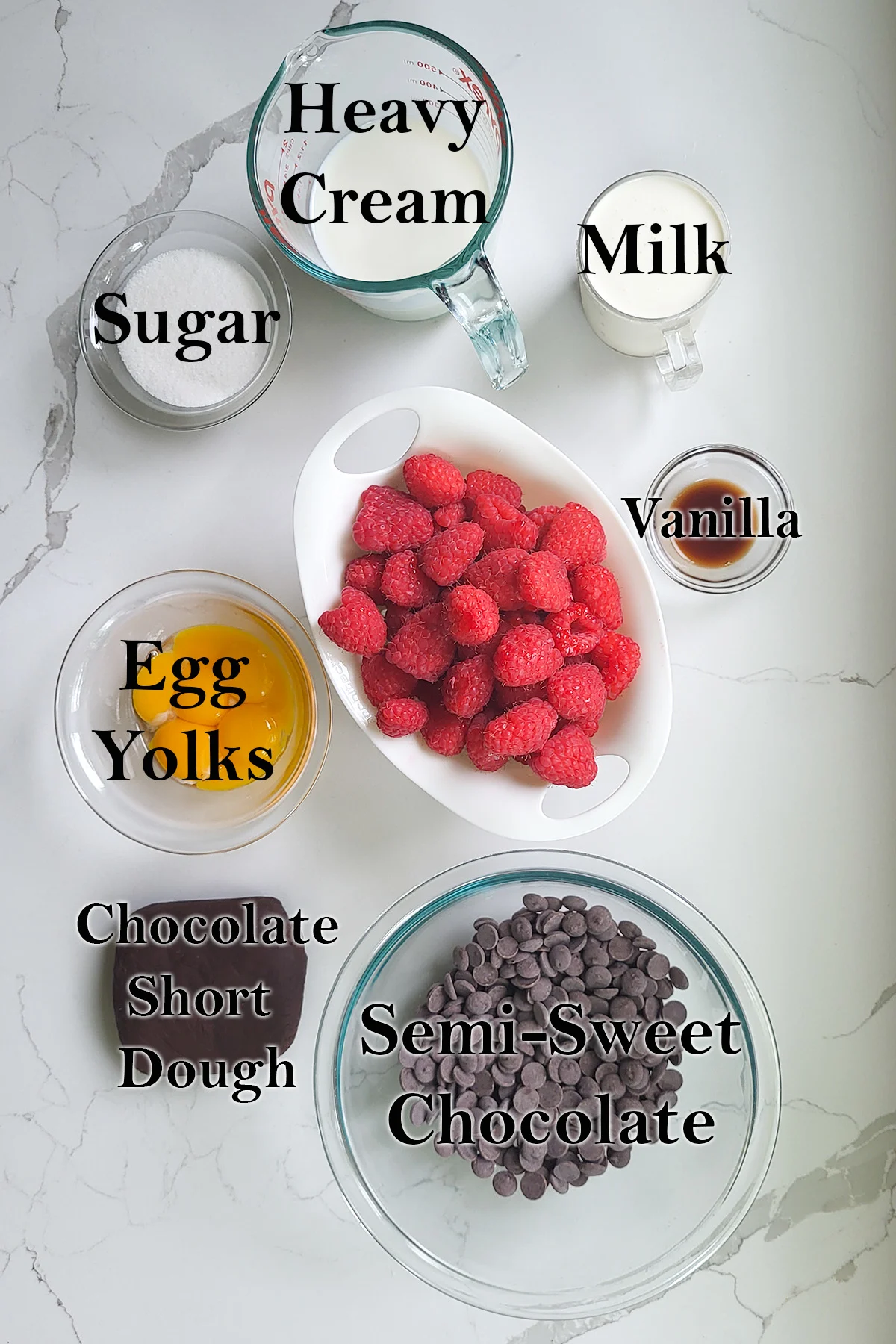 ingredients for chocolate raspberry tart in bowls on a white surface.