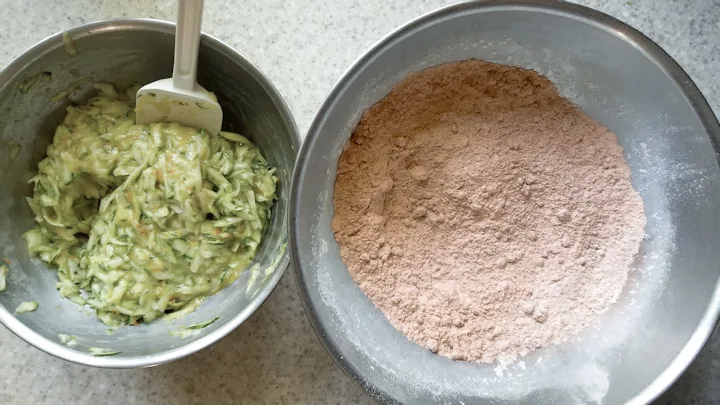 a bowl of dry ingredients and a bowl of wet ingredients with zucchini.